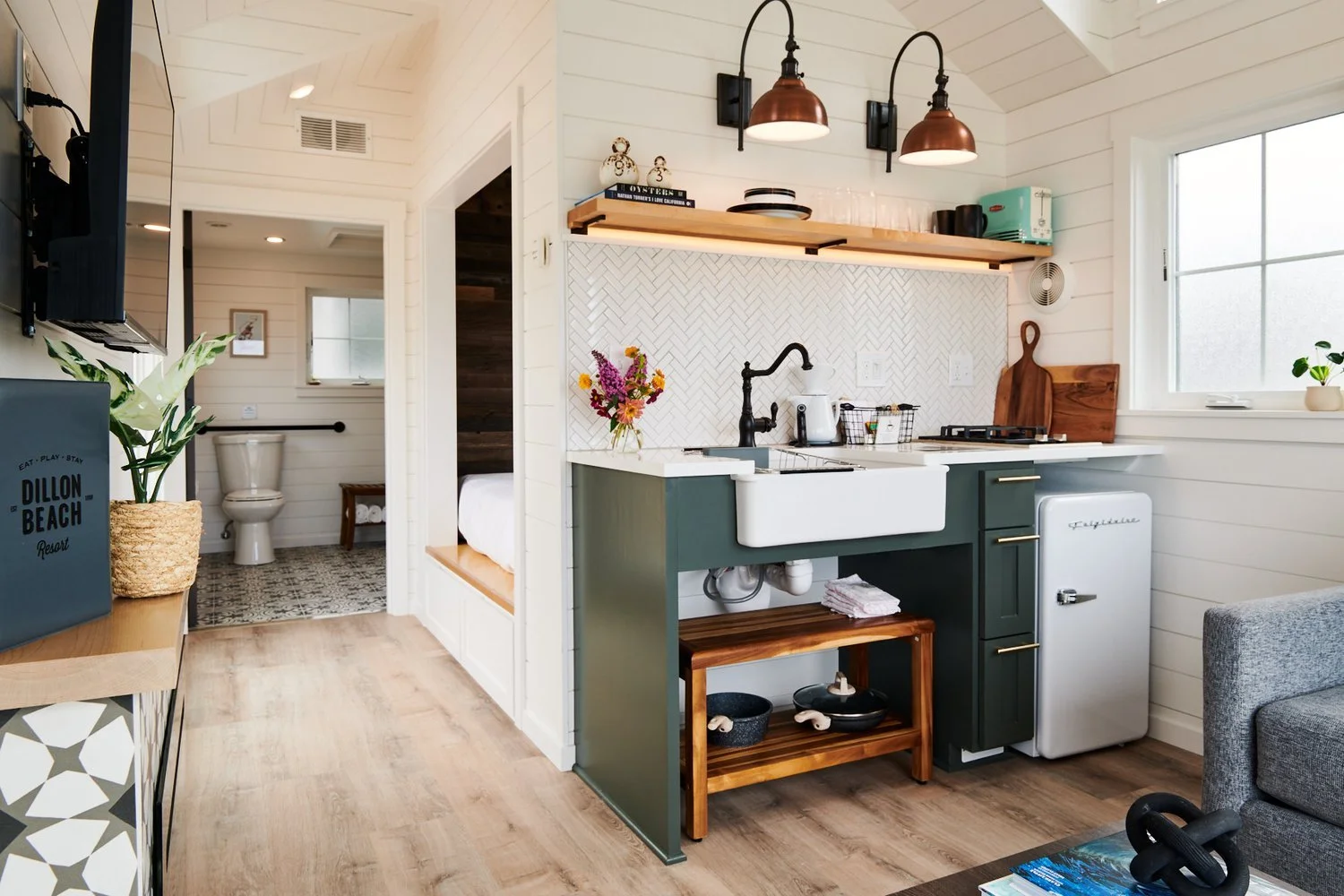 Modern tiny house at Dillon Beach Resort with forest green cabinets, farmhouse sink, and views of the bedroom and bath.