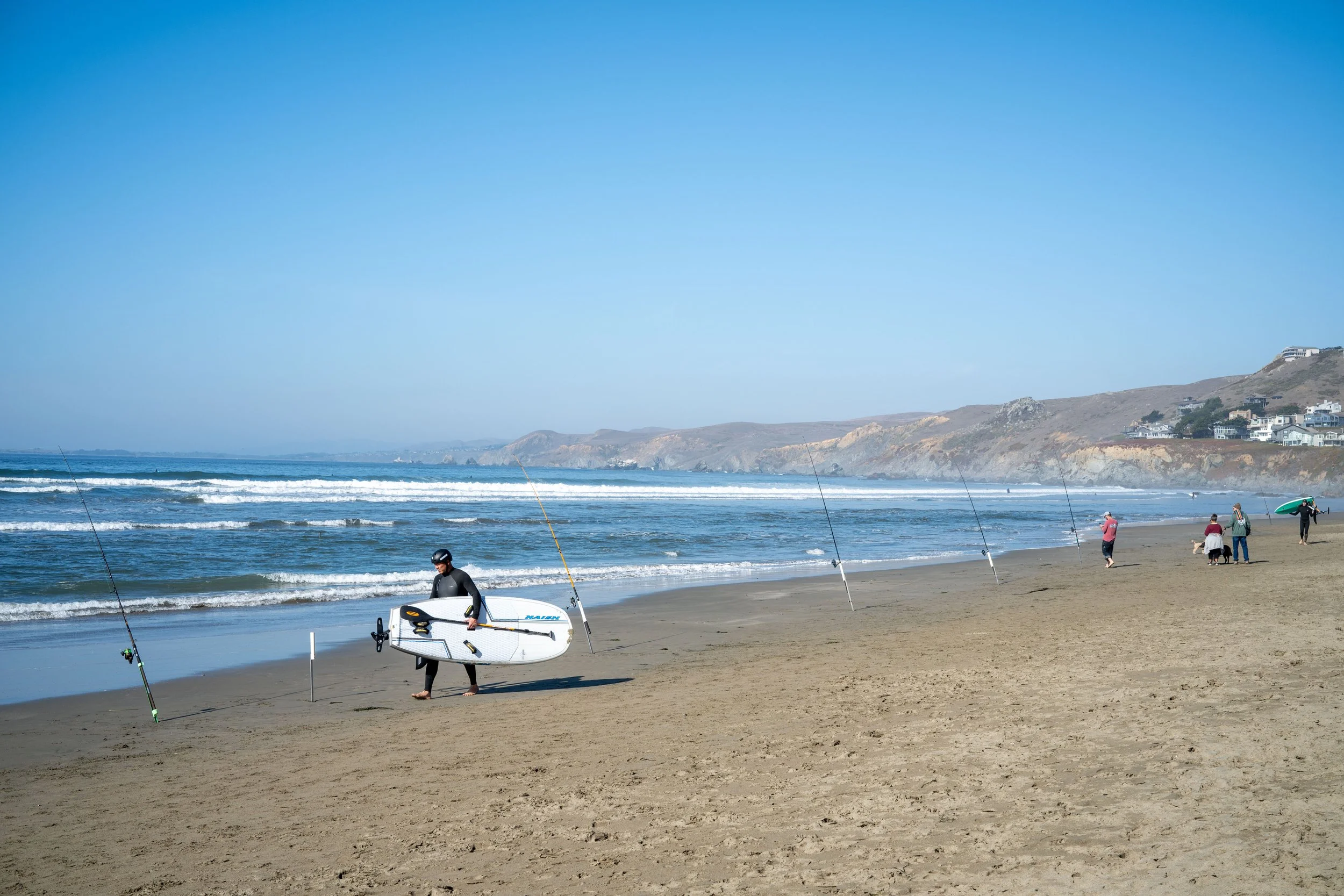 People on the beach preparing for or after kayaking, with the ocean waves and cliffs in the background.
