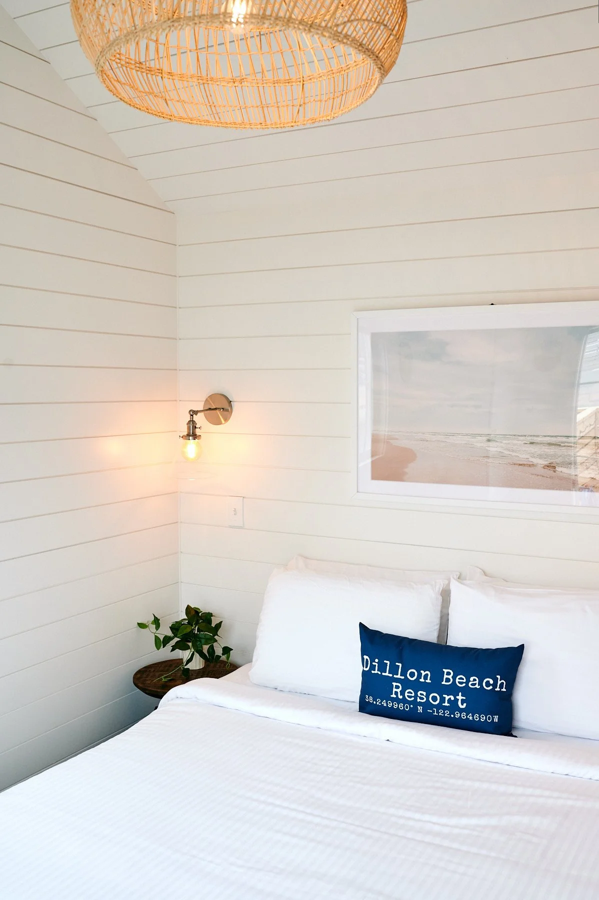 Dillon Beach Resort Sweetwater cabin. Inside, a mid-century modern cane-back chair with a patterned pillow sits on a natural wood live-edge side table next to an electric fireplace with graphic geometric tile.