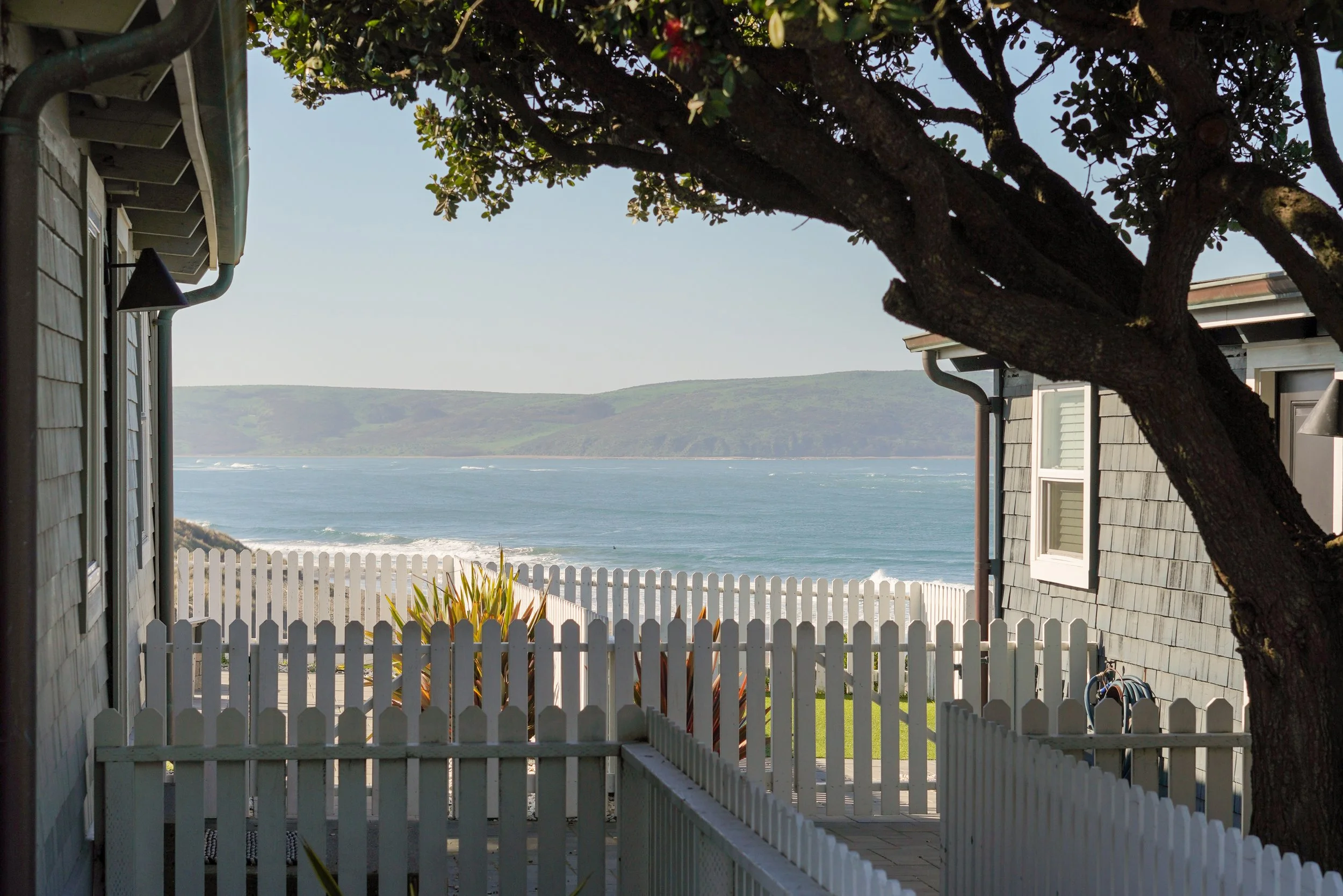 A row of modern, grey wood-sided cabins at Dillon Beach Resort, featuring private decks and coastal landscaping, ideal for overnight event guest lodging.