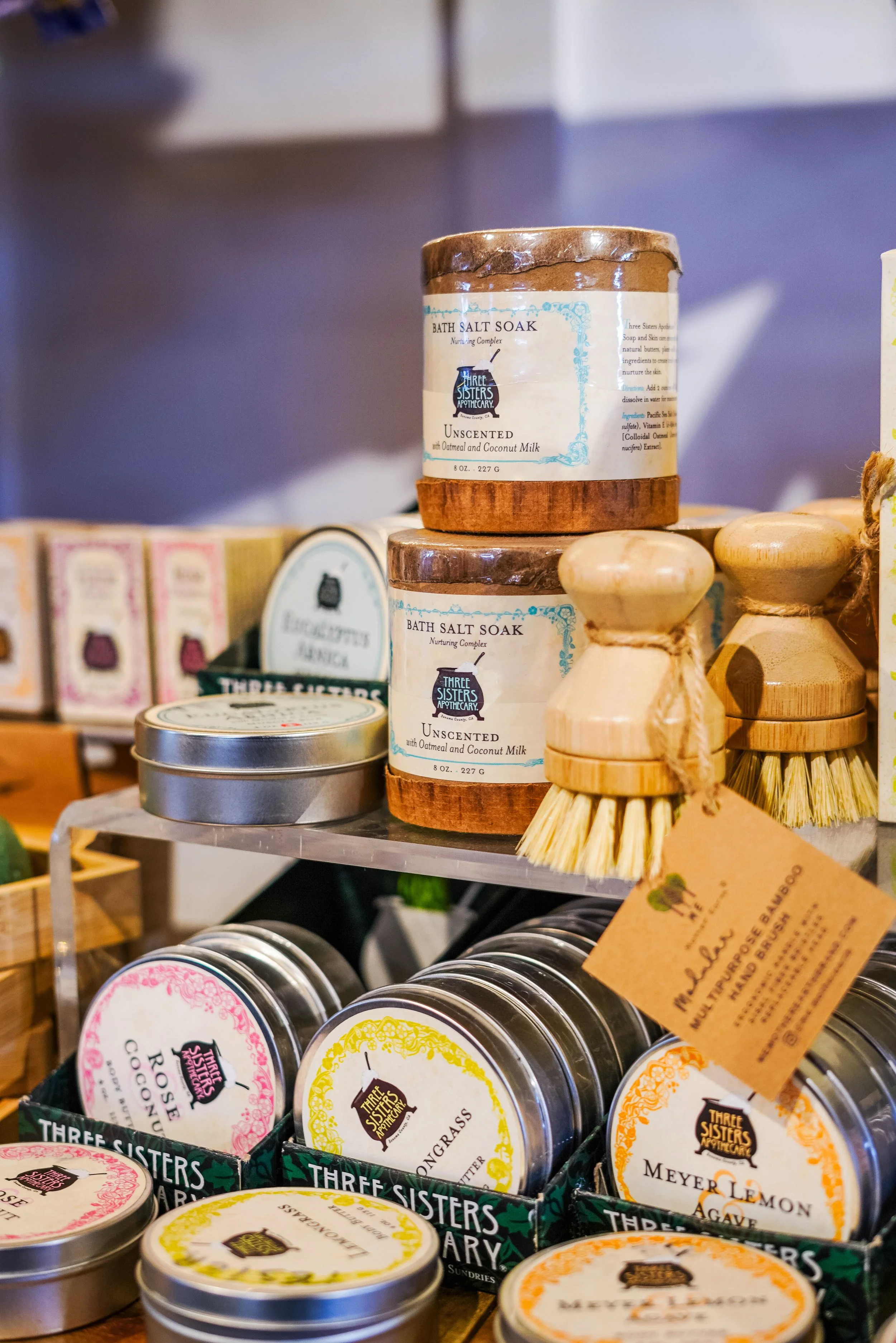 Stack of bath salt soak jars with wooden brushes on display in a store.