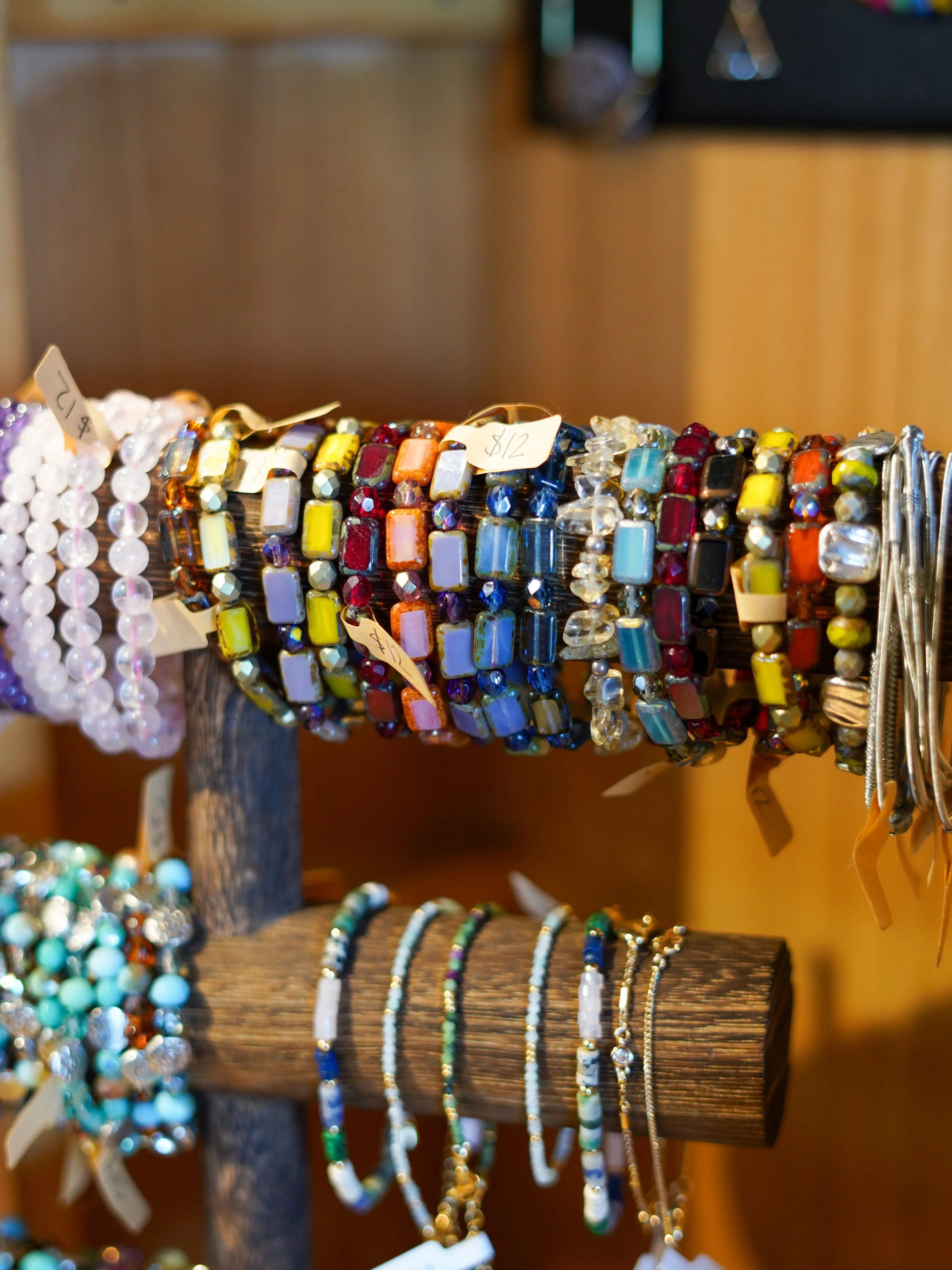 Colorful beaded bracelets and necklaces displayed on wooden stands at a craft fair.