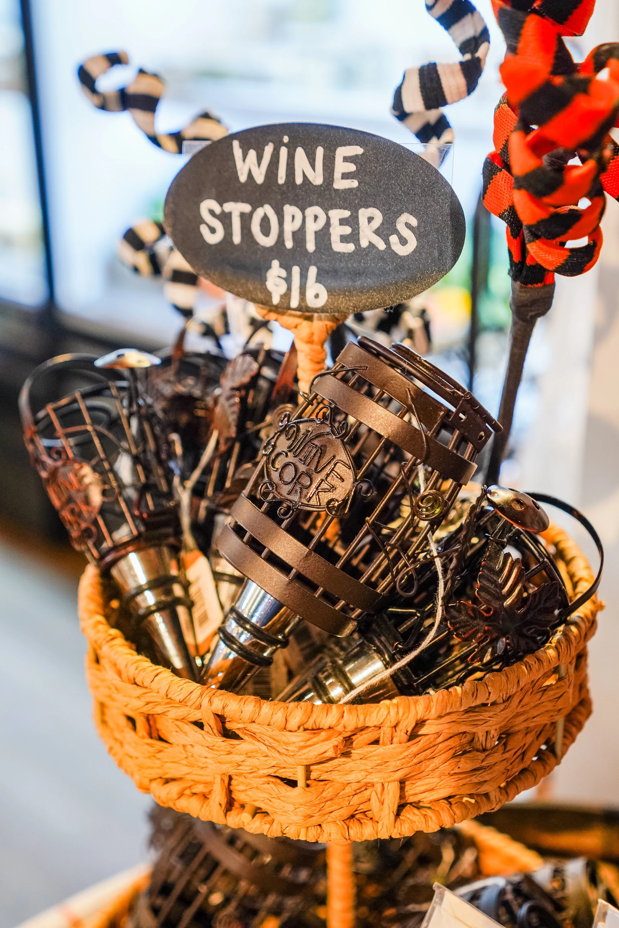 A small woven basket filled with miniature metal sculptures of motorcycles and a sign that reads 'Wine Stoppers $16' in white lettering on a black background.