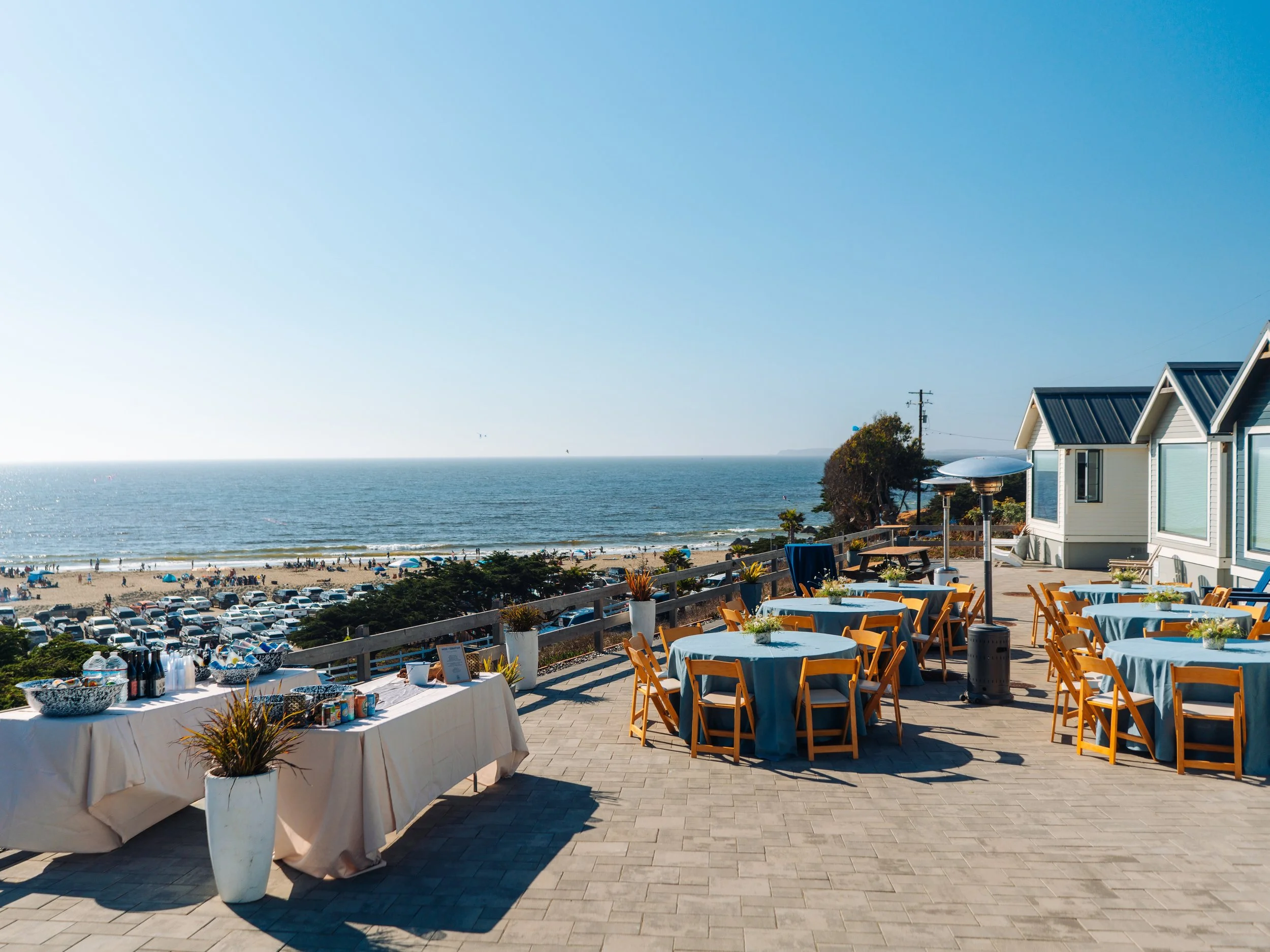 An elegant outdoor event table setting at Dillon Beach Resort, with wine glasses and floral arrangements glowing in the sunset light overlooking the ocean.