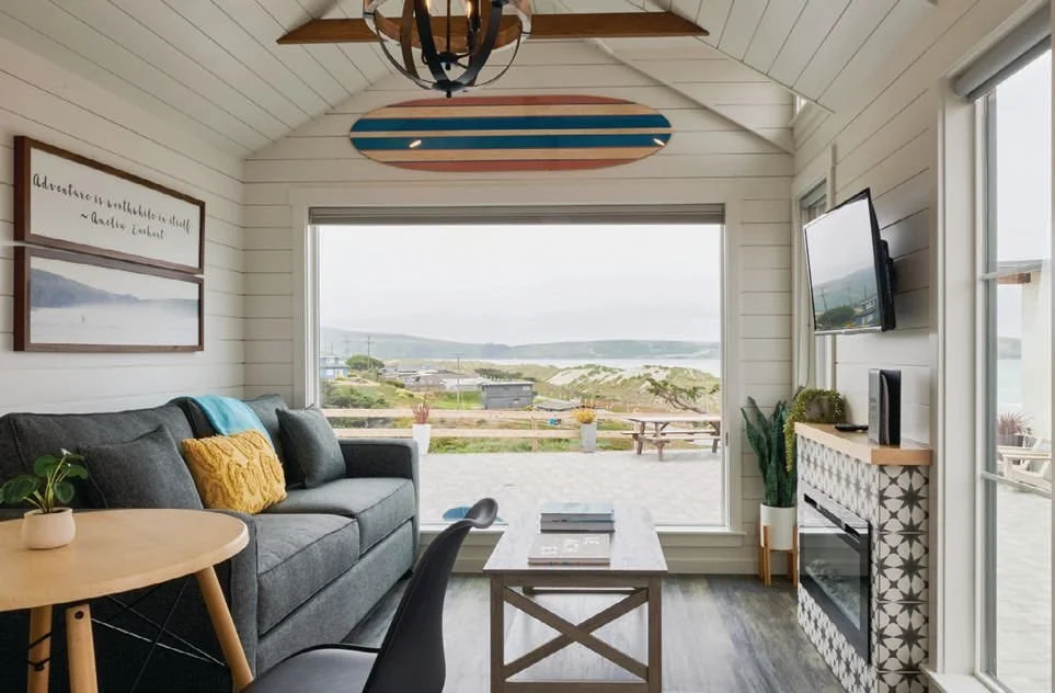 Bright tiny house living room with gray sofa and a large window overlooking the ocean and coast at Dillon Beach Resort.