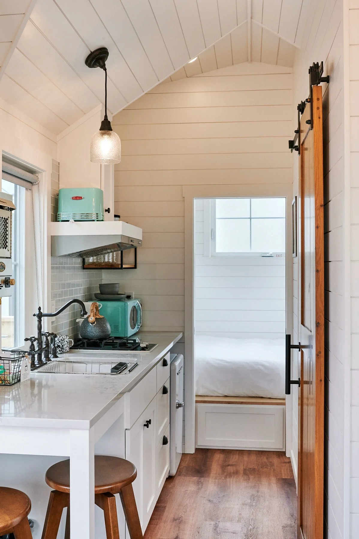 Tiny house kitchen at Dillon Beach Resort with teal appliances and a view into a cozy white-walled bedroom.