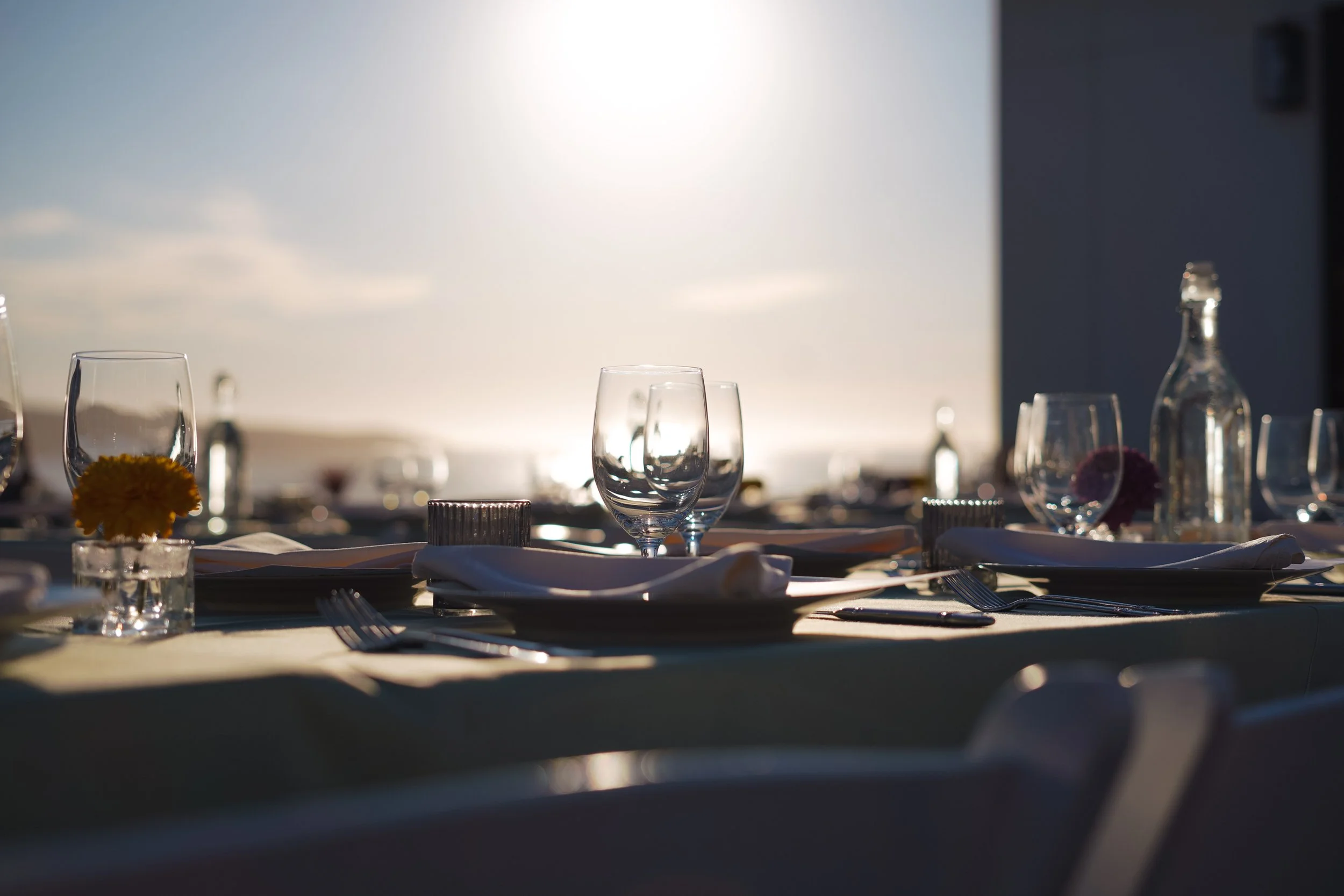 An elegant outdoor event table setting at Dillon Beach Resort, with wine glasses and floral arrangements glowing in the sunset light overlooking the ocean.