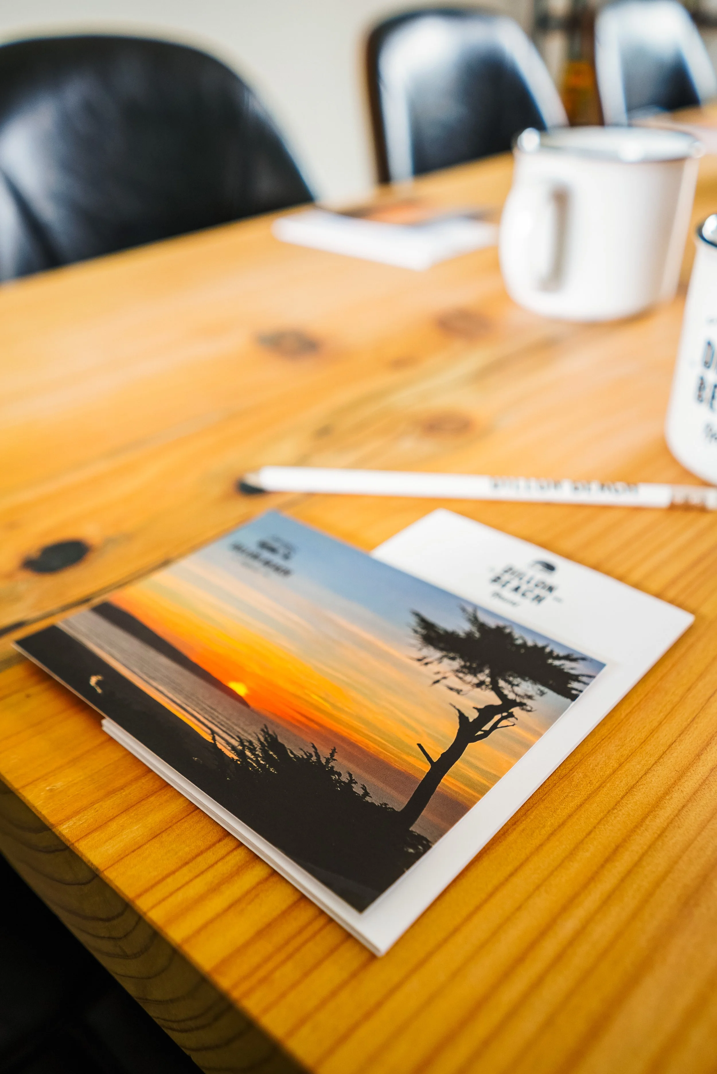 Close-up of Dillon Beach Resort stationery and a sunset postcard on a wood conference table for a corporate meeting.