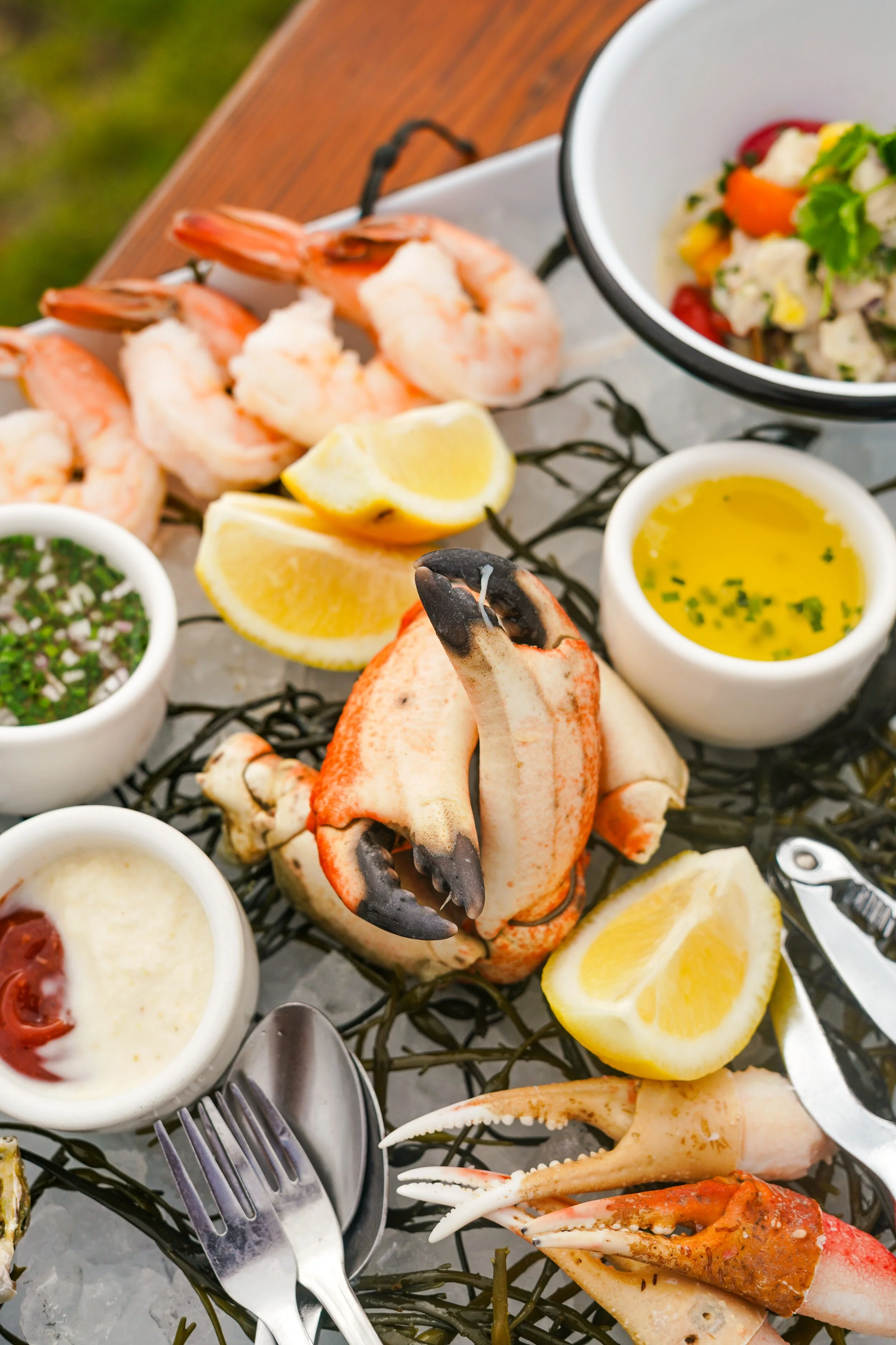 Seafood platter featuring shrimp, lobster, dipping sauces, lemon wedges, and side salad with vegetables