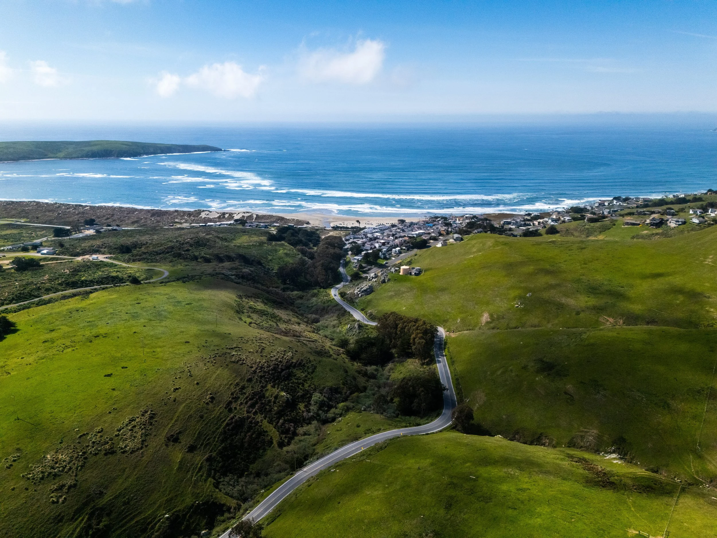 An aerial drone view of Dillon Beach Resort’s modern cottages and event grounds, located directly on the coastline with waves crashing on the sandy beach below.