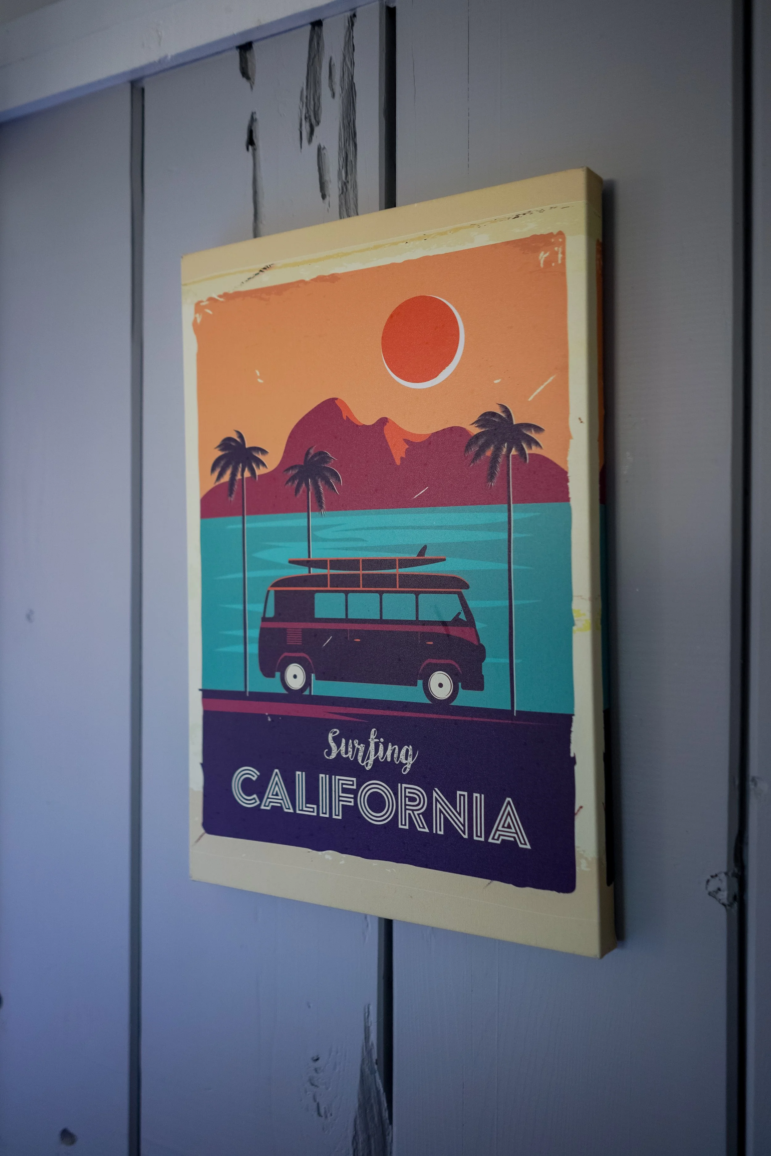 Close-up of a vintage-style 'Surfing California' art print featuring a surf van and palm trees against a sunset background.