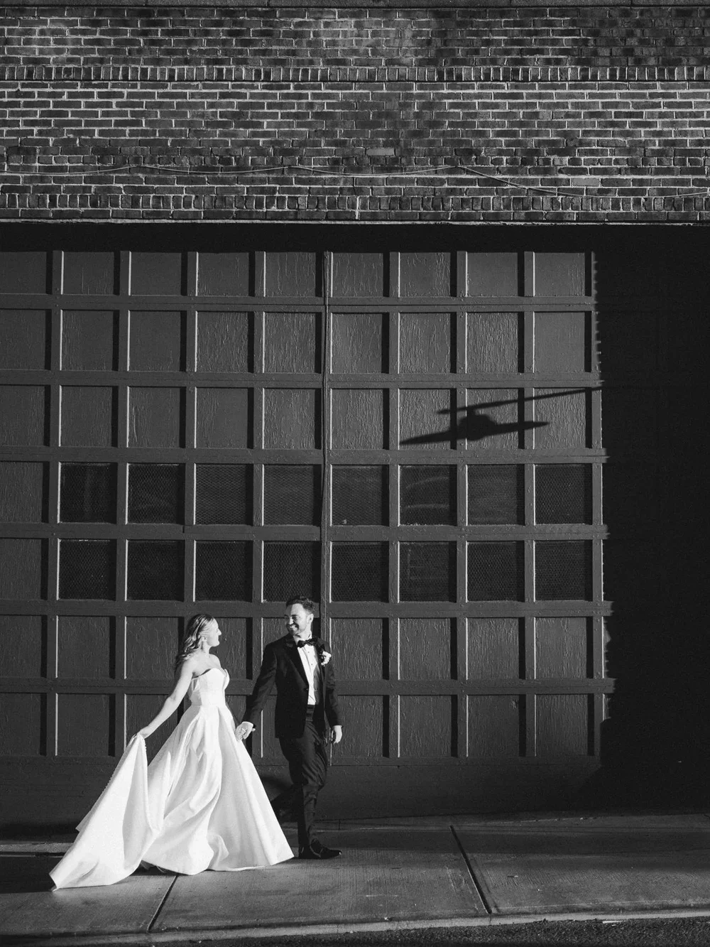 Bride and groom walking hand in hand in front of modern brick architecture, Knoxville city wedding