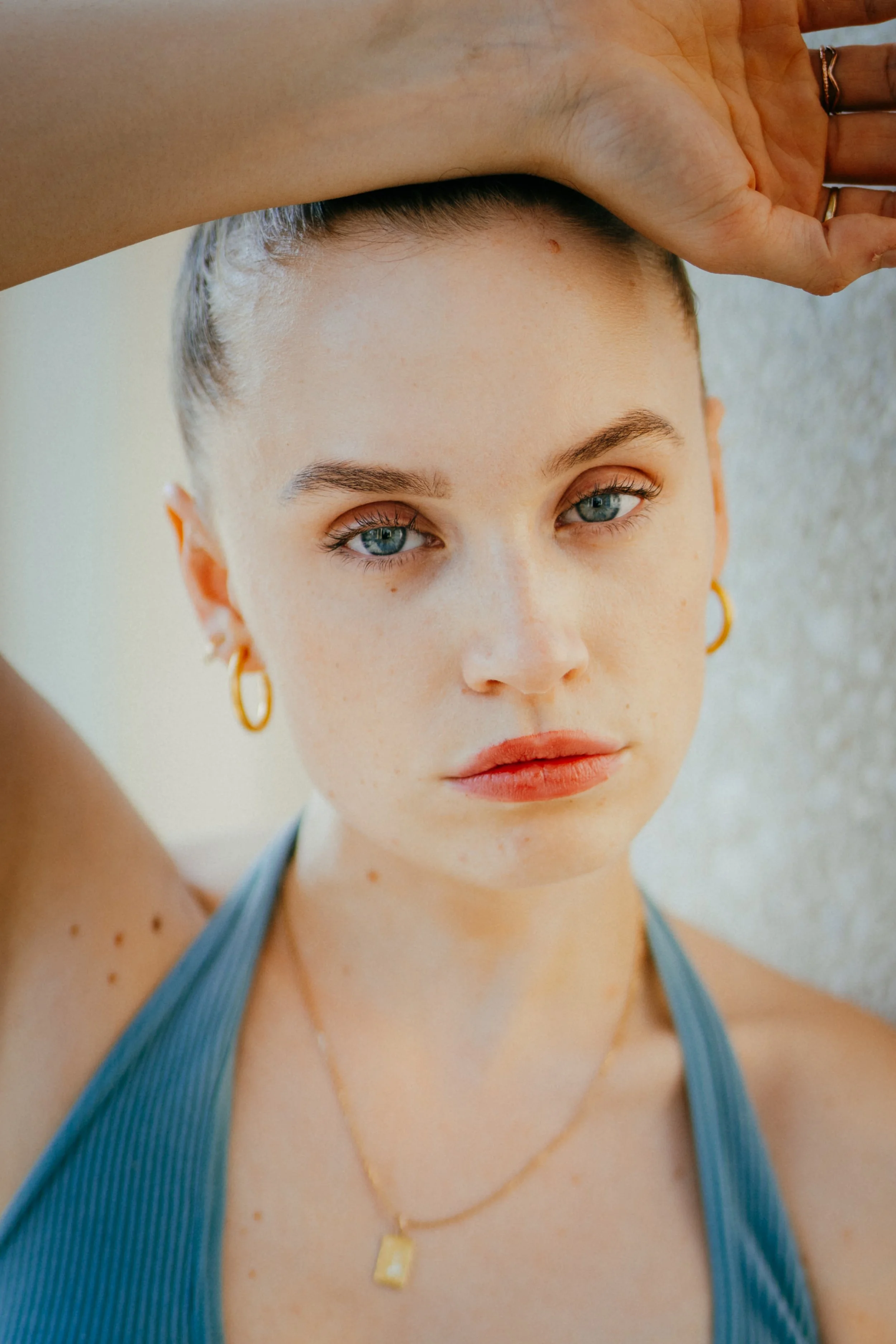 Nahaufnahme eines jungen Mädchens mit blonden Haaren, blauen Augen, goldenen Ohrringen und zwei goldenen Halsketten, die einen blauen Sport-BH trägt.