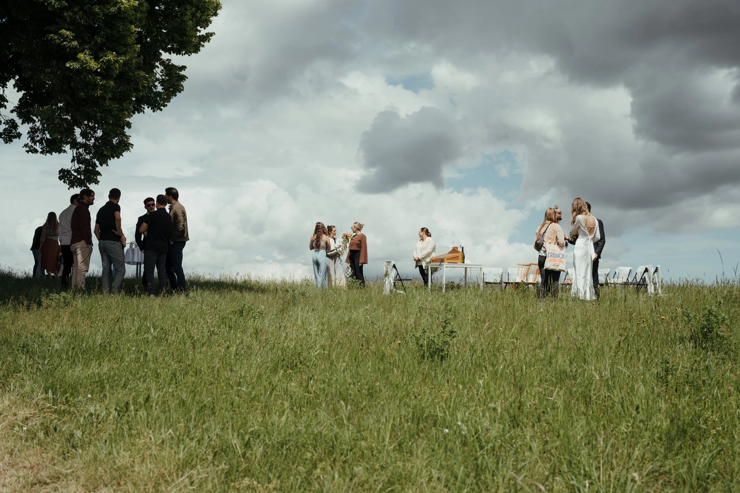 Gruppe von Menschen, die sich bei einer Outdoor-Veranstaltung im Gras unter einem bewölkten Himmel versammelt haben.