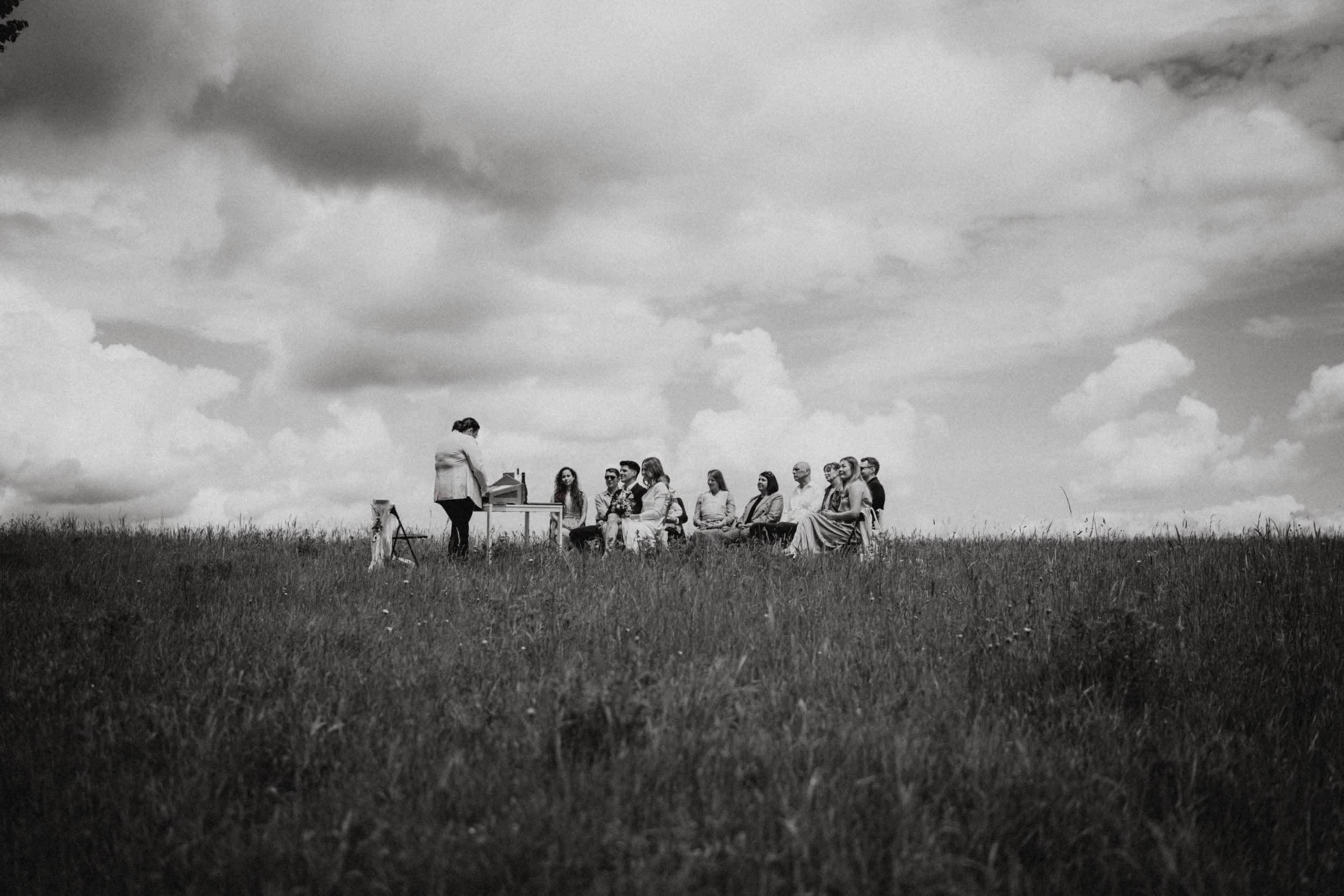 Eine schwarze und weiße Aufnahme einer Gruppe von Menschen, die im Freien auf einem Feld sitzen, während eine einzelne Person vor ihnen steht.