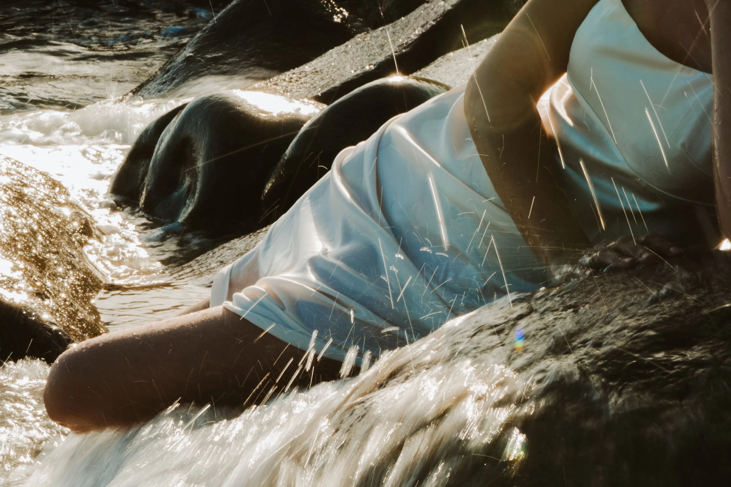 Nahaufnahme von Wasser, das über glatte Steine in einem Fluss fließt, mit Sonnenlicht, das auf die Wasseroberfläche reflektiert.