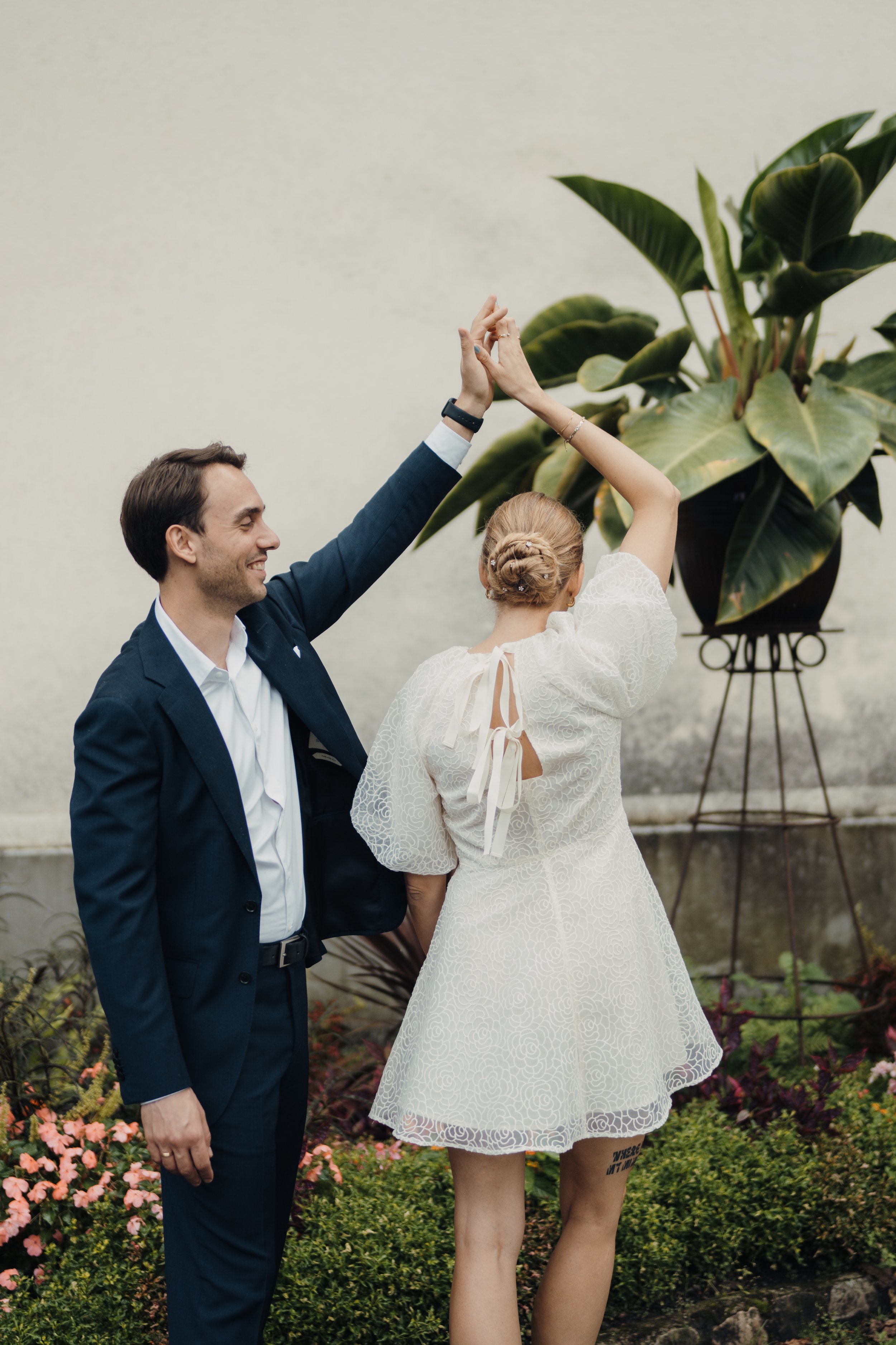 Ein Mann und eine Frau tanzen zusammen in einem Garten, umgeben von Blumen und Pflanzen, bei einer Hochzeit oder einem Fest.