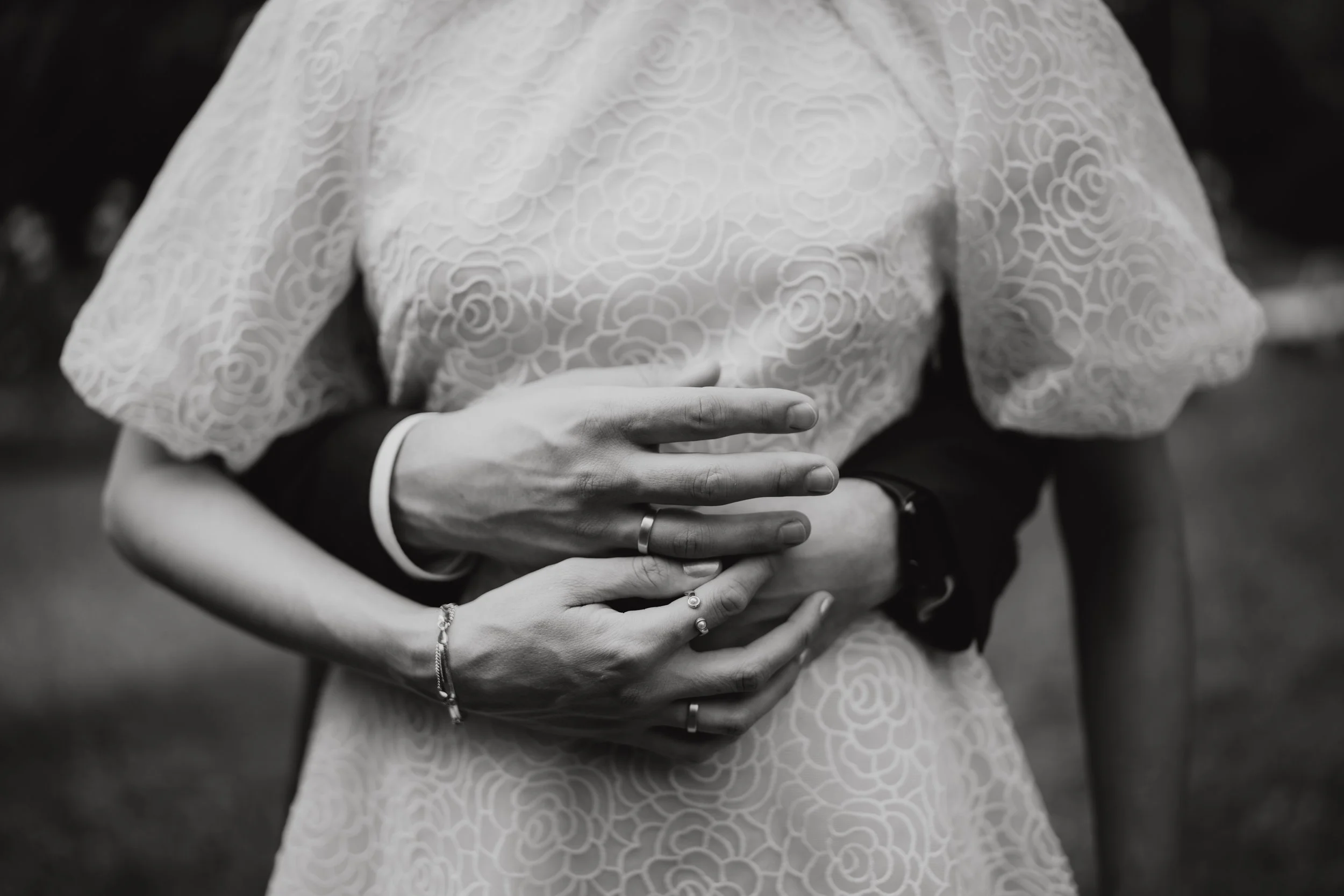 Zwei Personen umarmen sich auf einer Hochzeit, eine trägt ein Spitzenkleid, die Hände sind sichtbar.