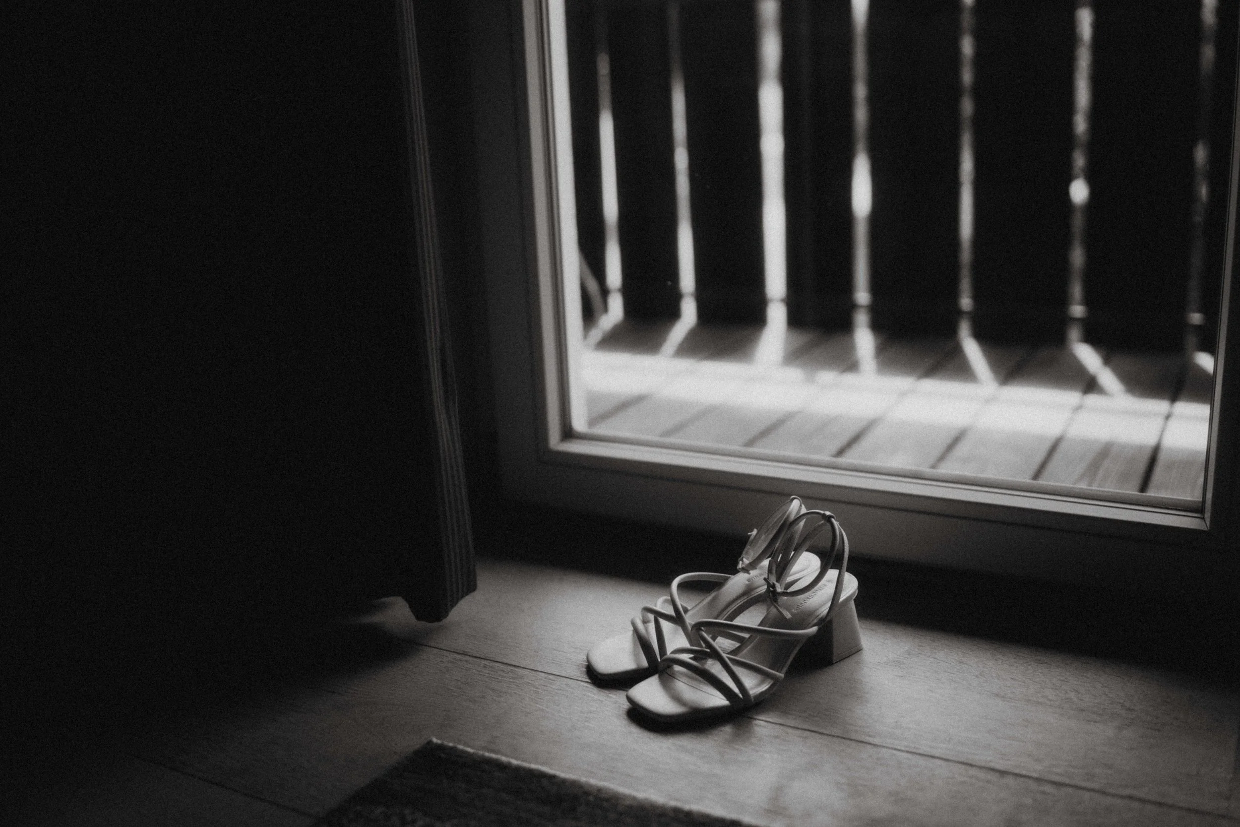 Schwarze Schuhe neben einem Fenster mit Gitter und Sonnenlicht, das durch die Gitter scheint.