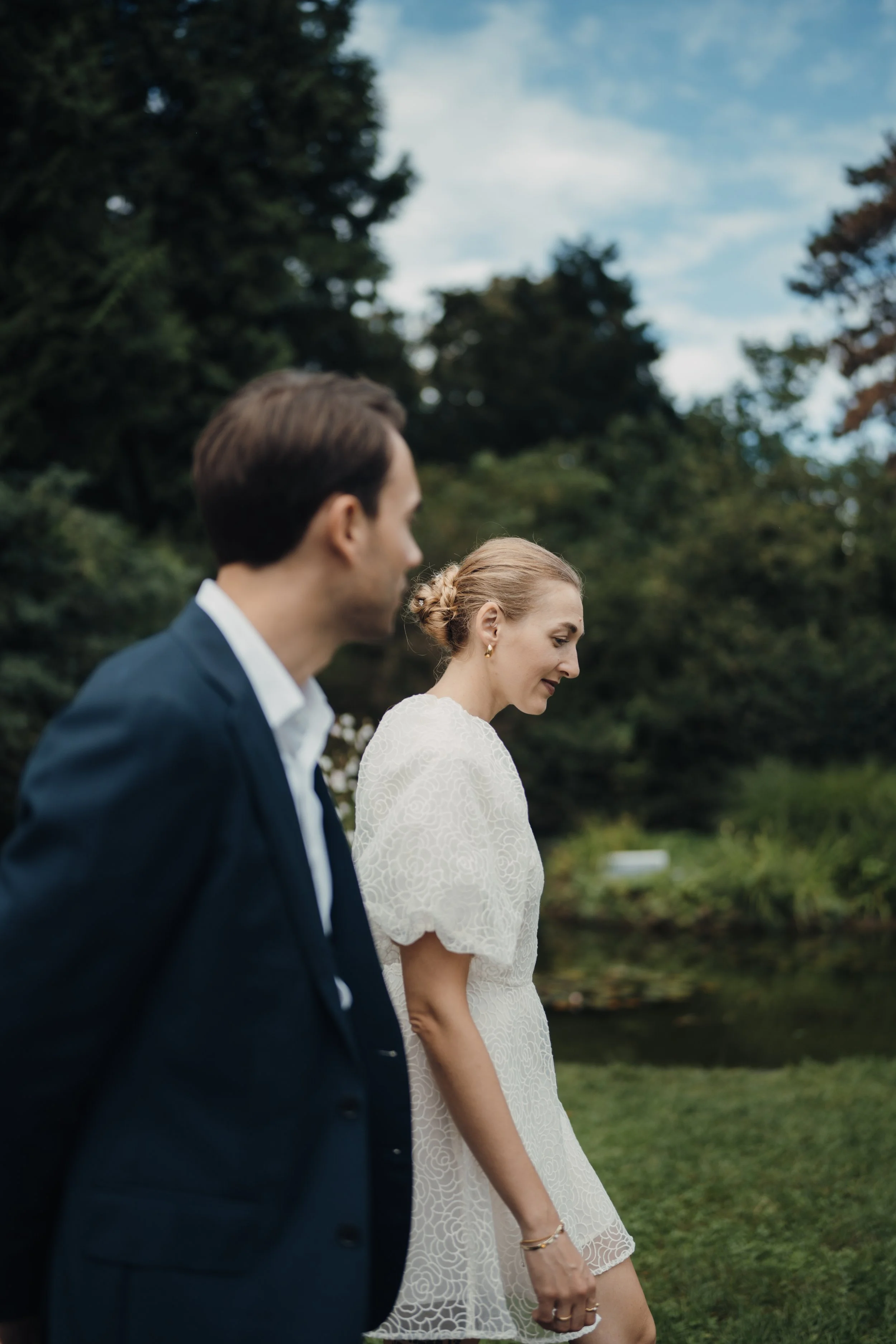 Ein Mann und eine Frau bei einer Zeremonie im Freien, umgeben von Bäumen und Himmel, im Fokus auf die Frau in einem weißen Kleid.