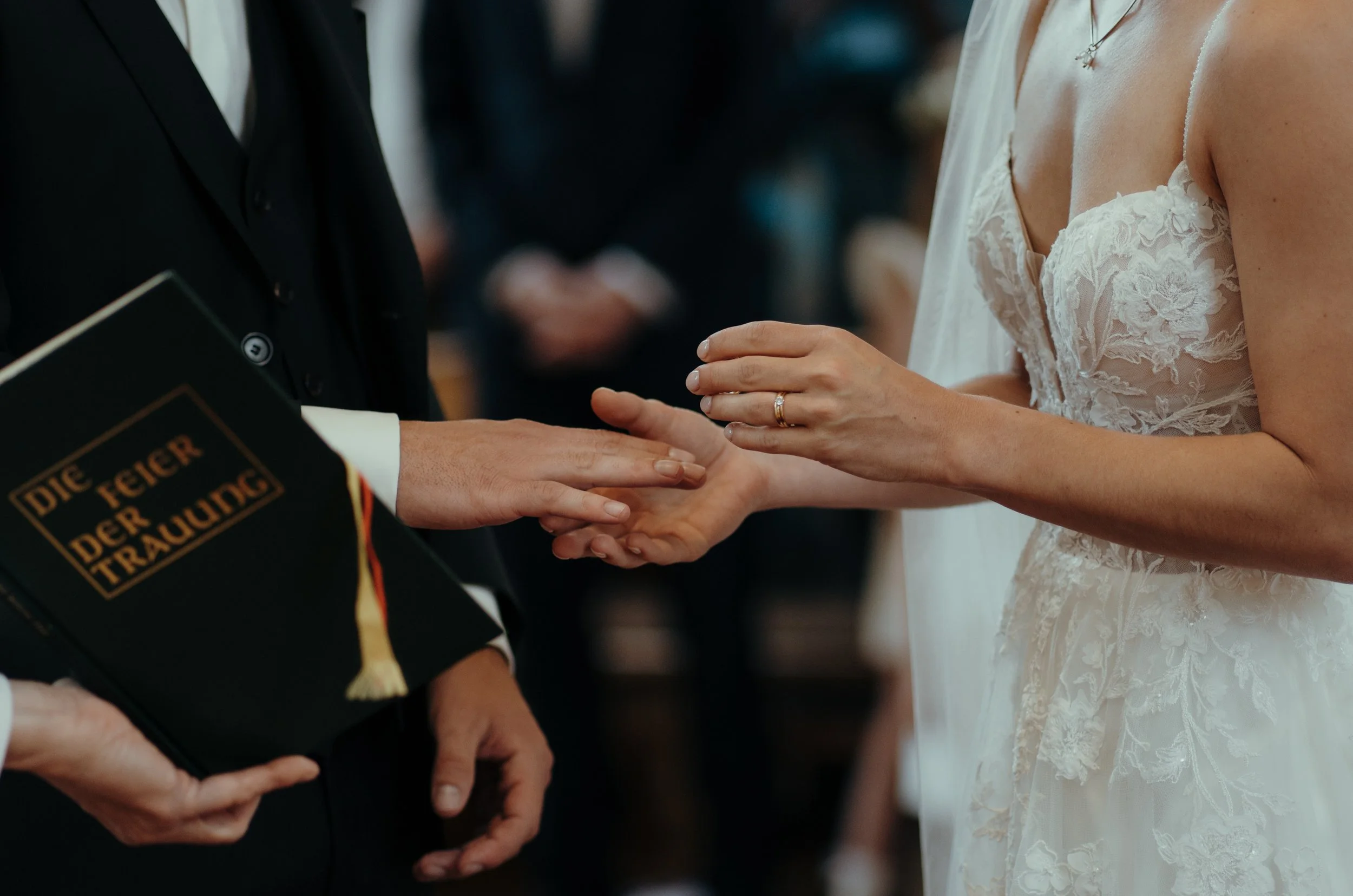 Hochzeitspaar hält sich an den Händen, die Braut trägt ein weißes Spitzenkleid, der Bräutigam trägt einen schwarzen Anzug.