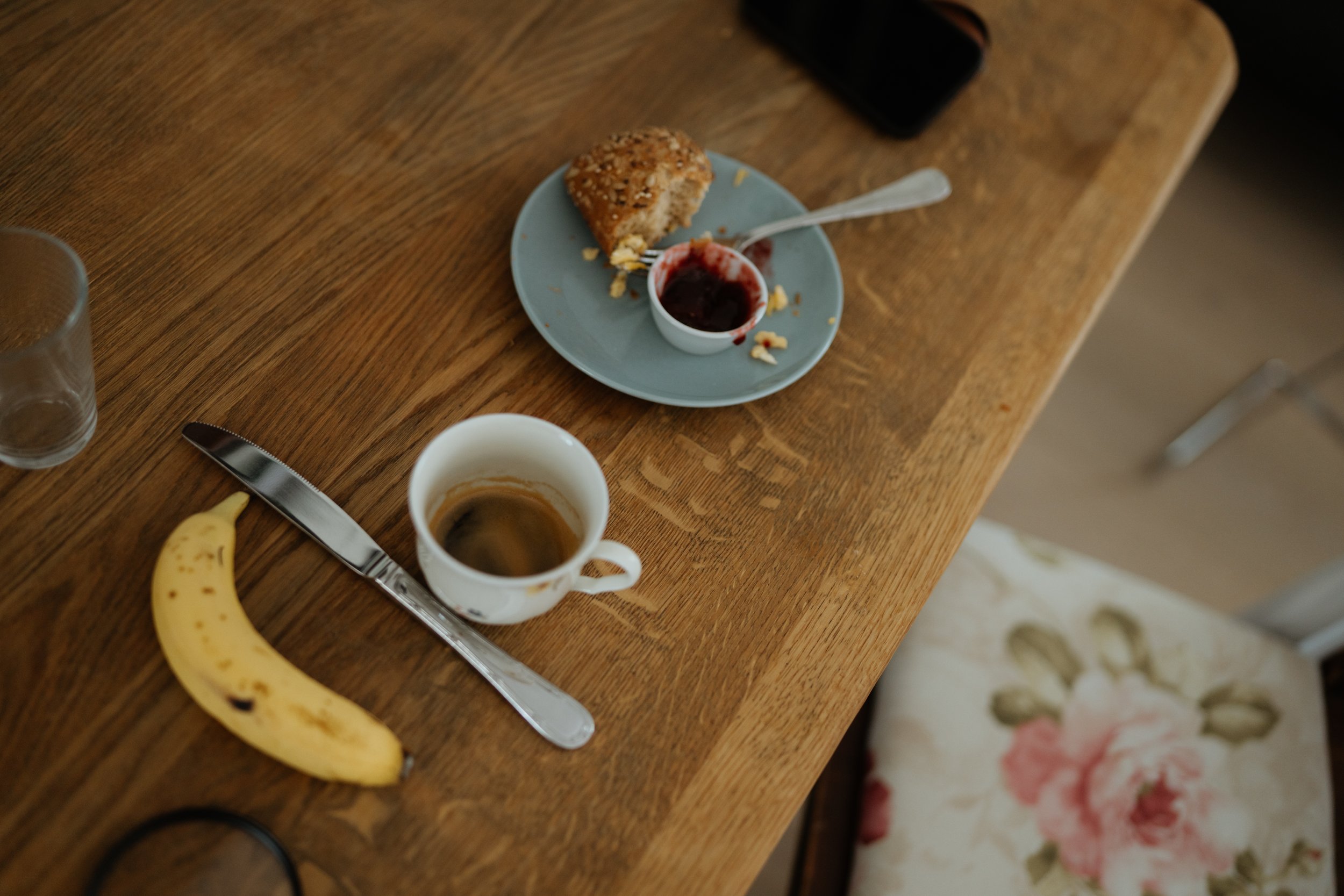 Halb gefressener Kuchen auf einem blauen Teller mit Beerenkompott. Neben dem Teller eine Tasse Kaffee, ein Messer, eine Banane und ein halb leeres Glas.