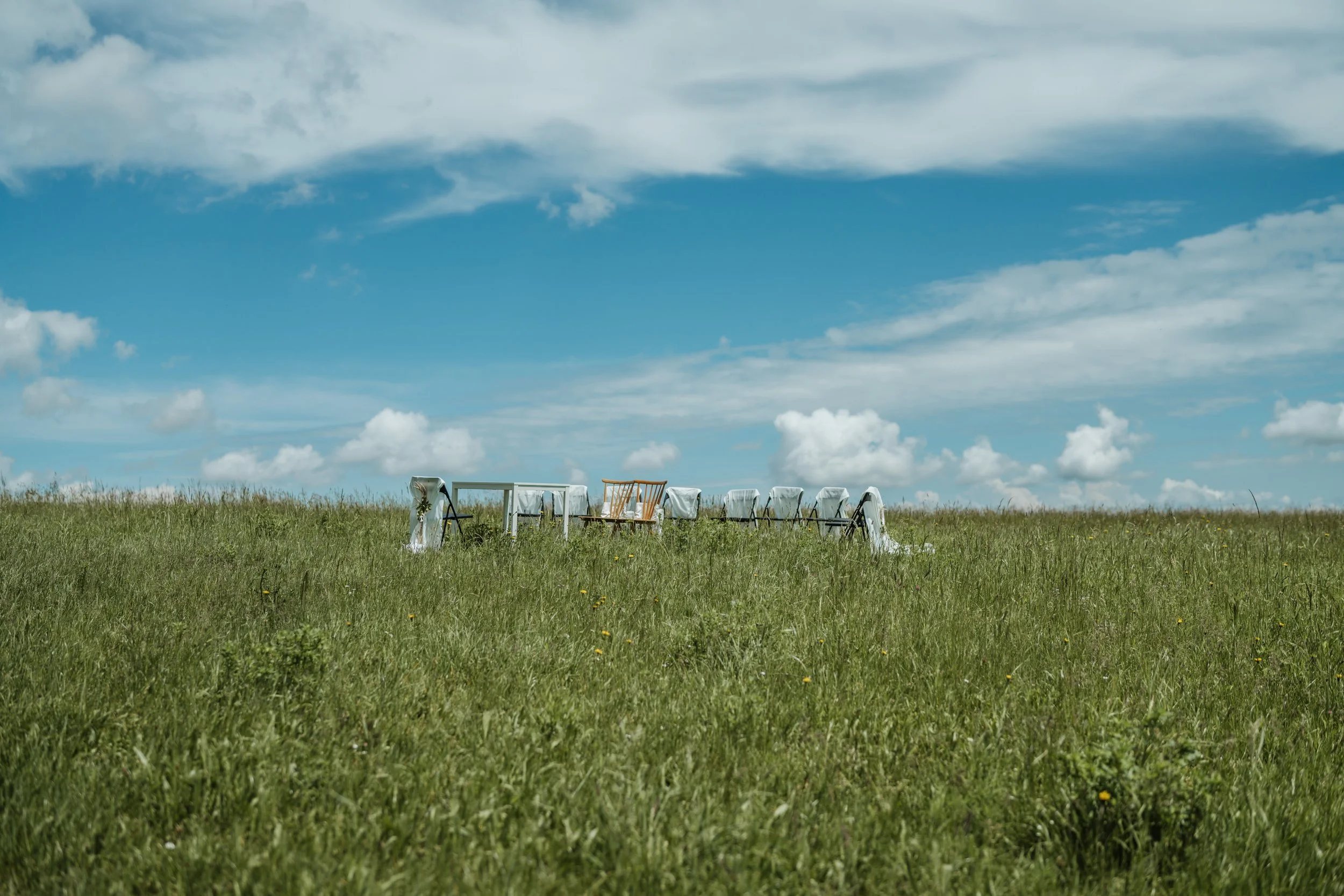 Ein offenes Feld mit mehreren weißen und braunen Sitzgelegenheiten und einem Tisch unter einem blauen Himmel mit Wolken.