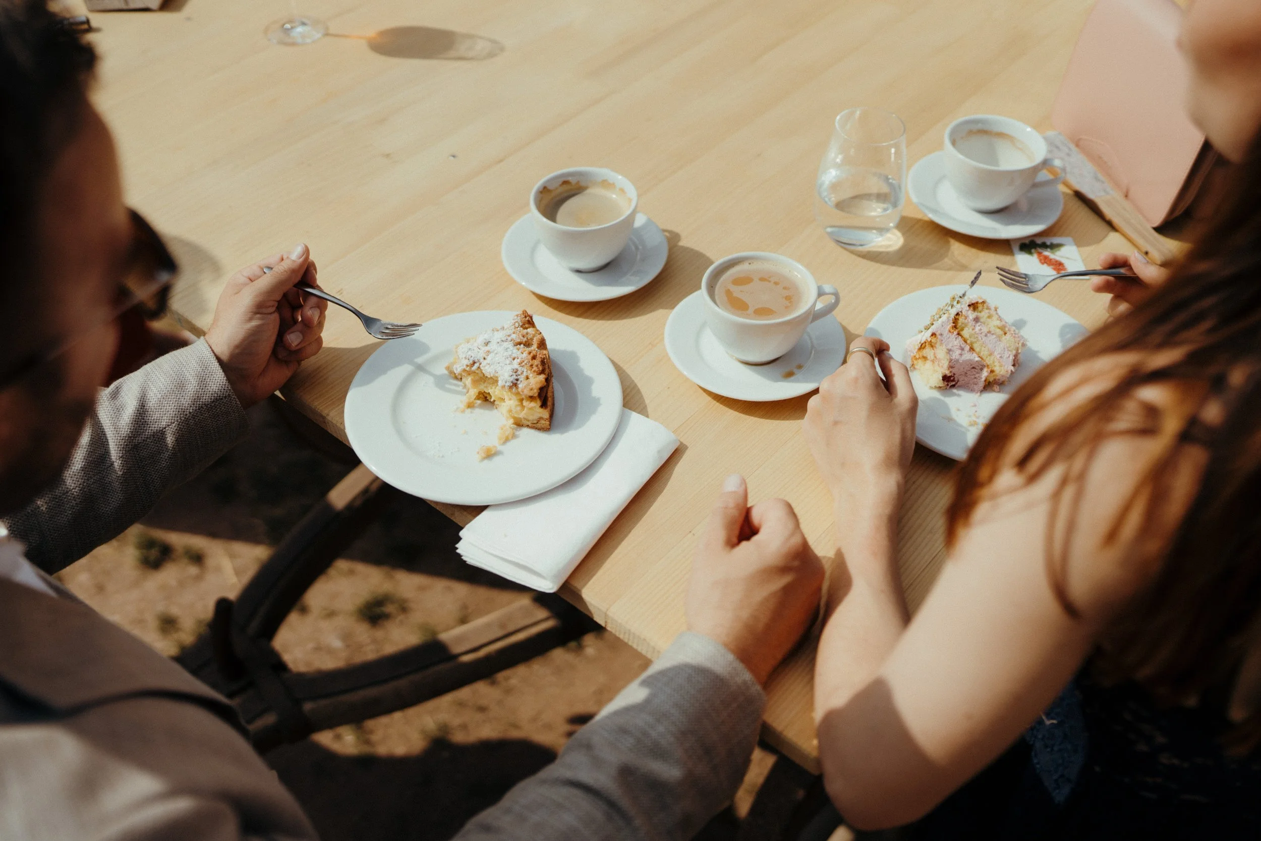 Mehrere Menschen sitzen an einem Holztisch, essen Kuchen und trinken Kaffee, während sie sich Unterhalten.
