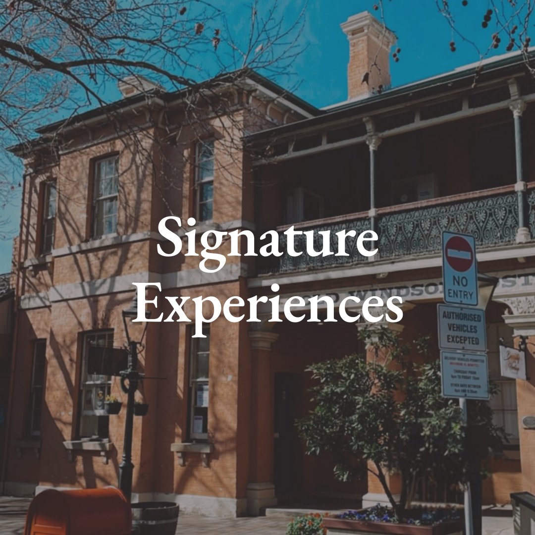 A historic brick building with ornate balcony and a no entry street sign in front. Shadows of leafless tree branches fall on the building, and a clear blue sky is behind.