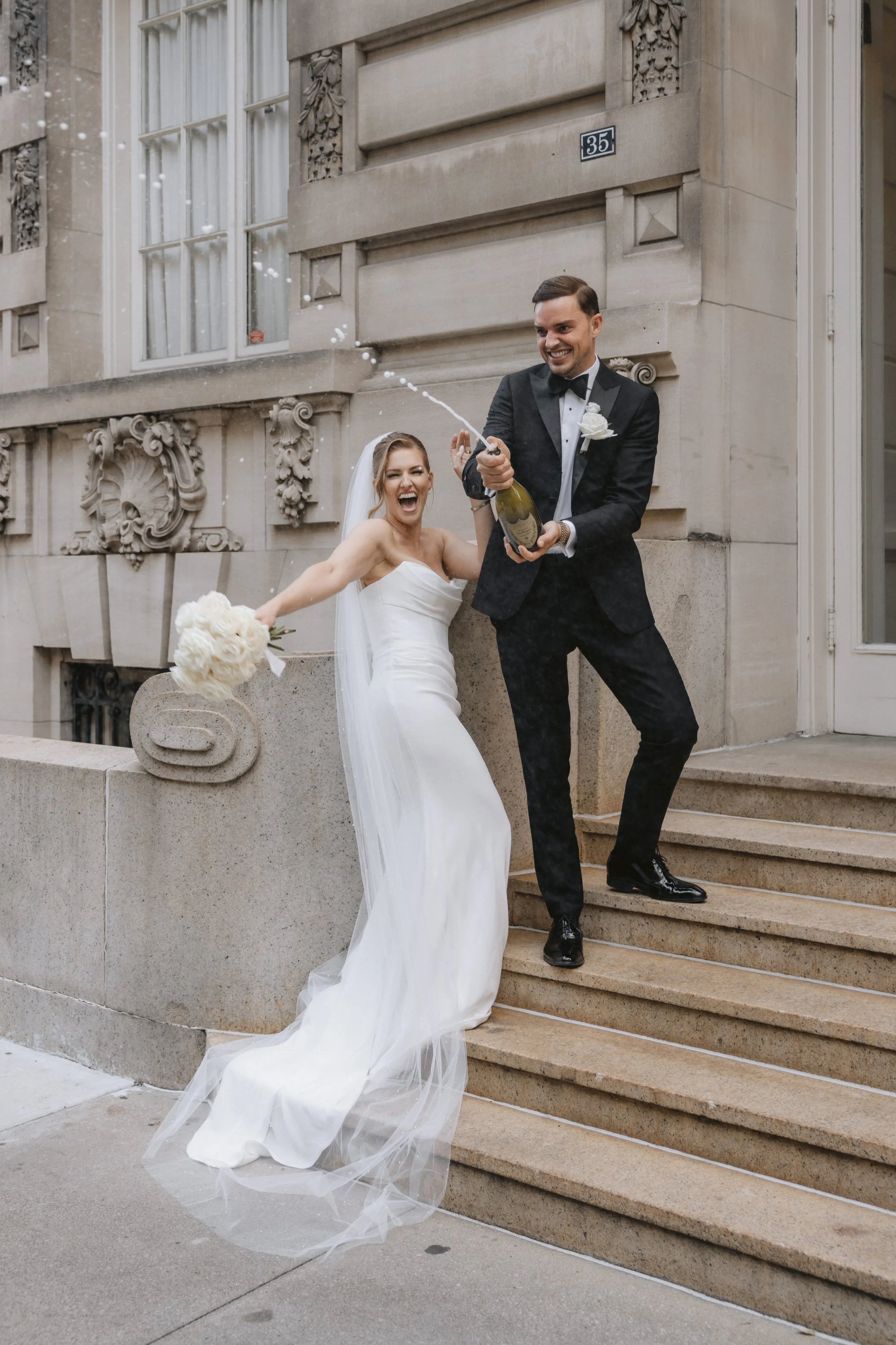 Luxury elopement in New York City. Groom and bride are celebrating with champagne and classic bridal bouquet of white roses