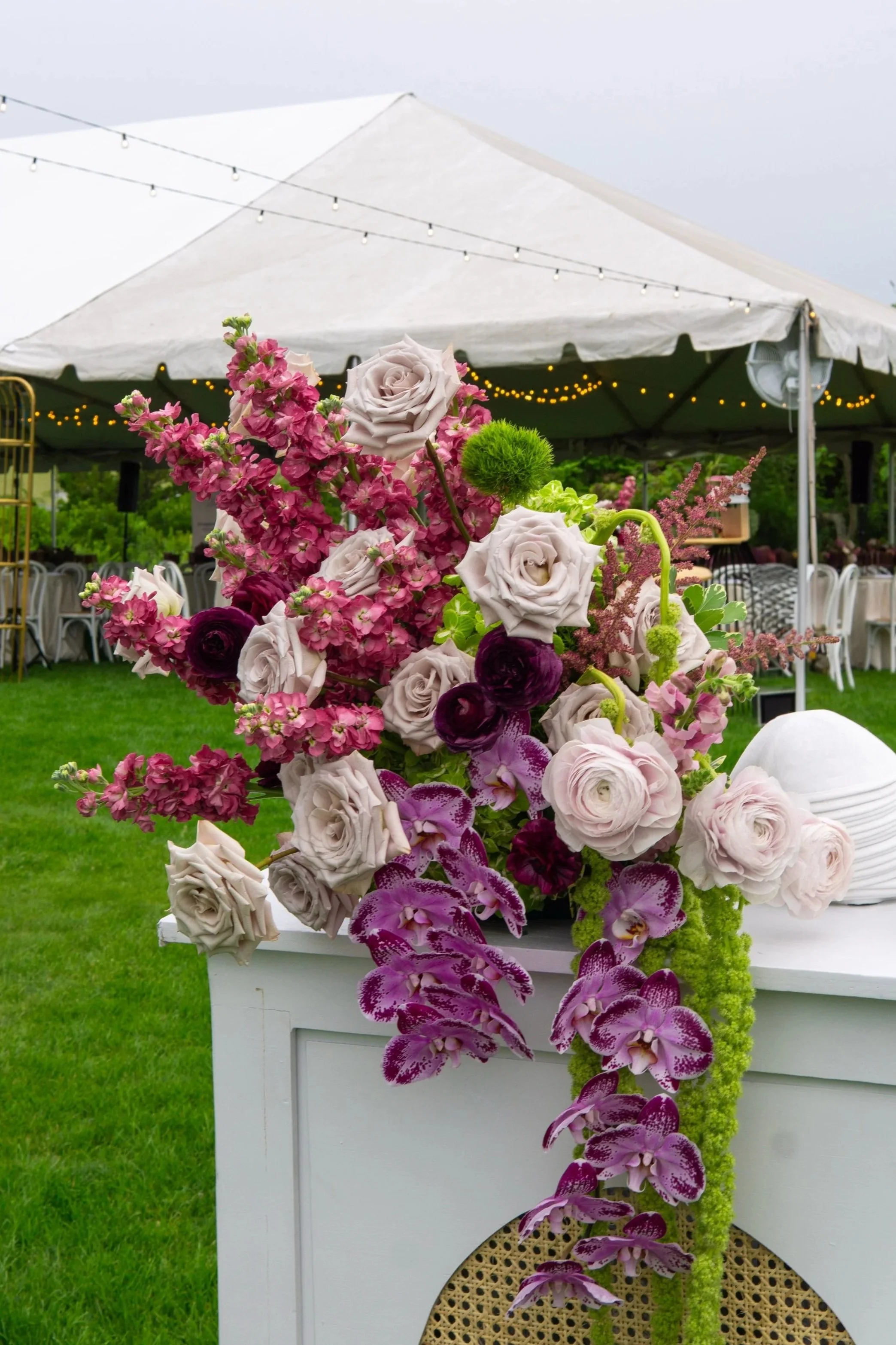 A colorful floral arrangement with roses, orchids, ranunculus, stock flower, hanging green amaranth in Hamptons