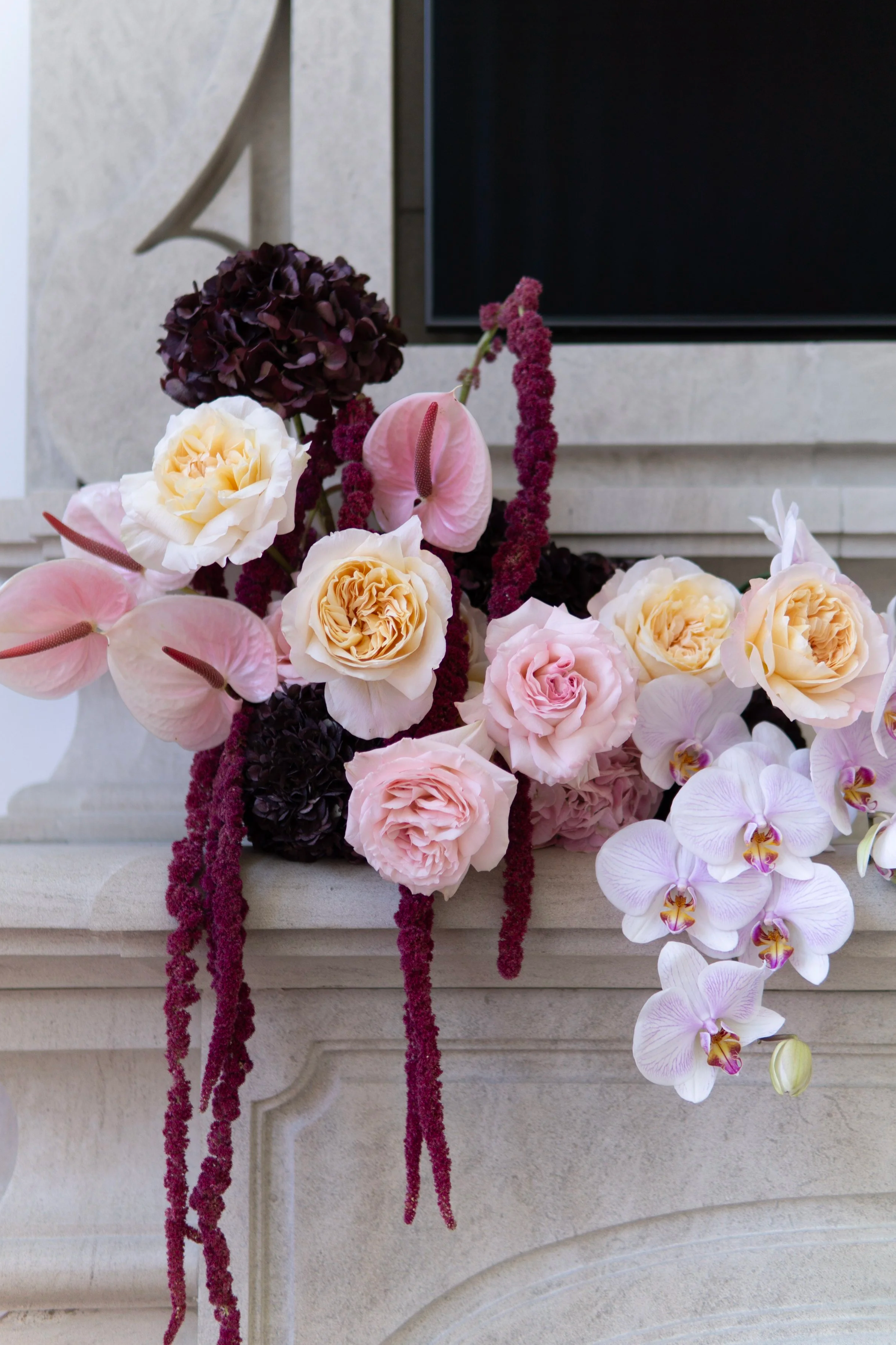 Sculptural floral arrangement placed on a mantel featuring premium dark hydrangeas, pink anthuriums, orchids and roses