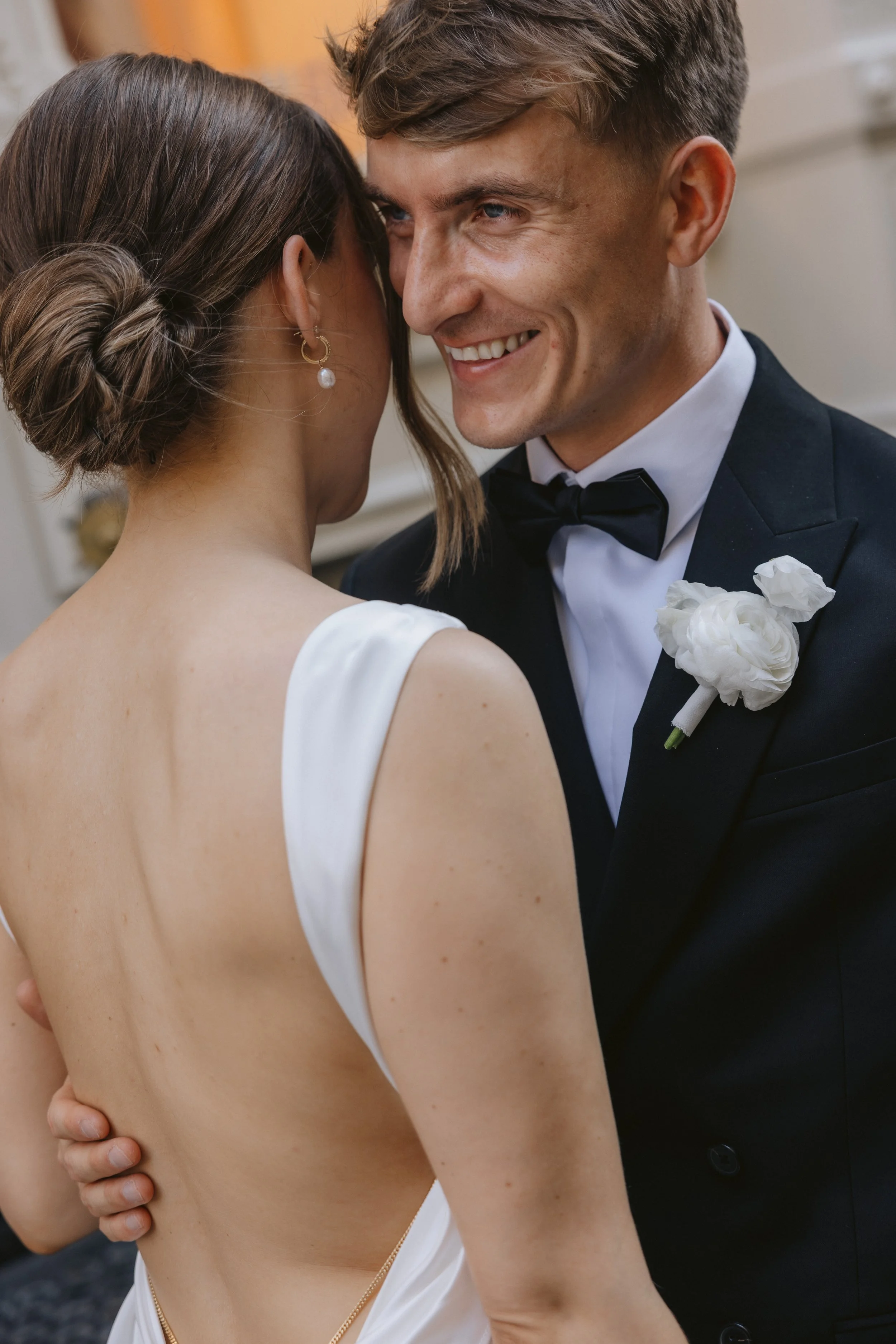 The groom is wearing an elegant white flower boutonniere, made with ranunculus and sweet pea