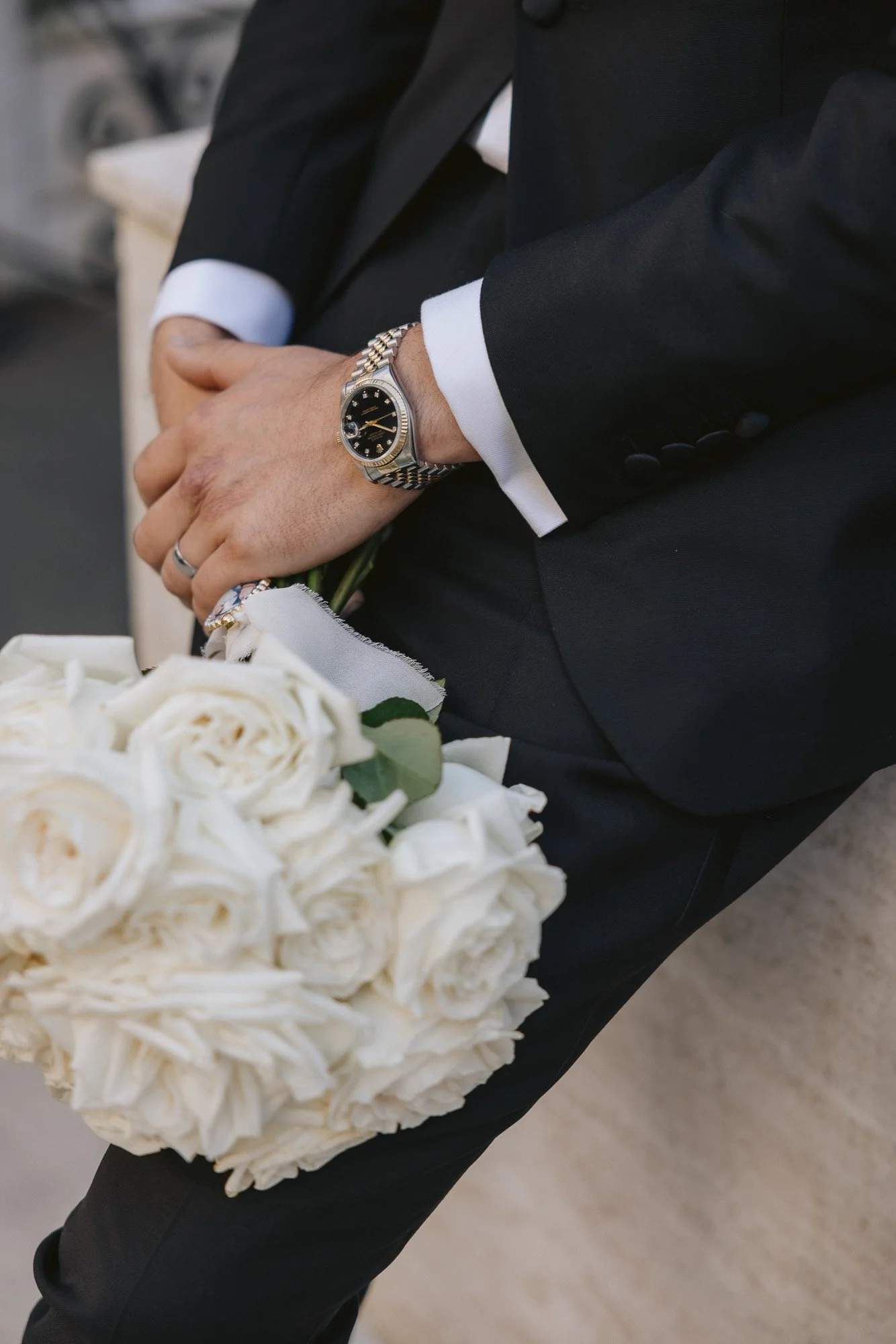 Close-up of a man in a black suit holding a bridal bouquet of white roses