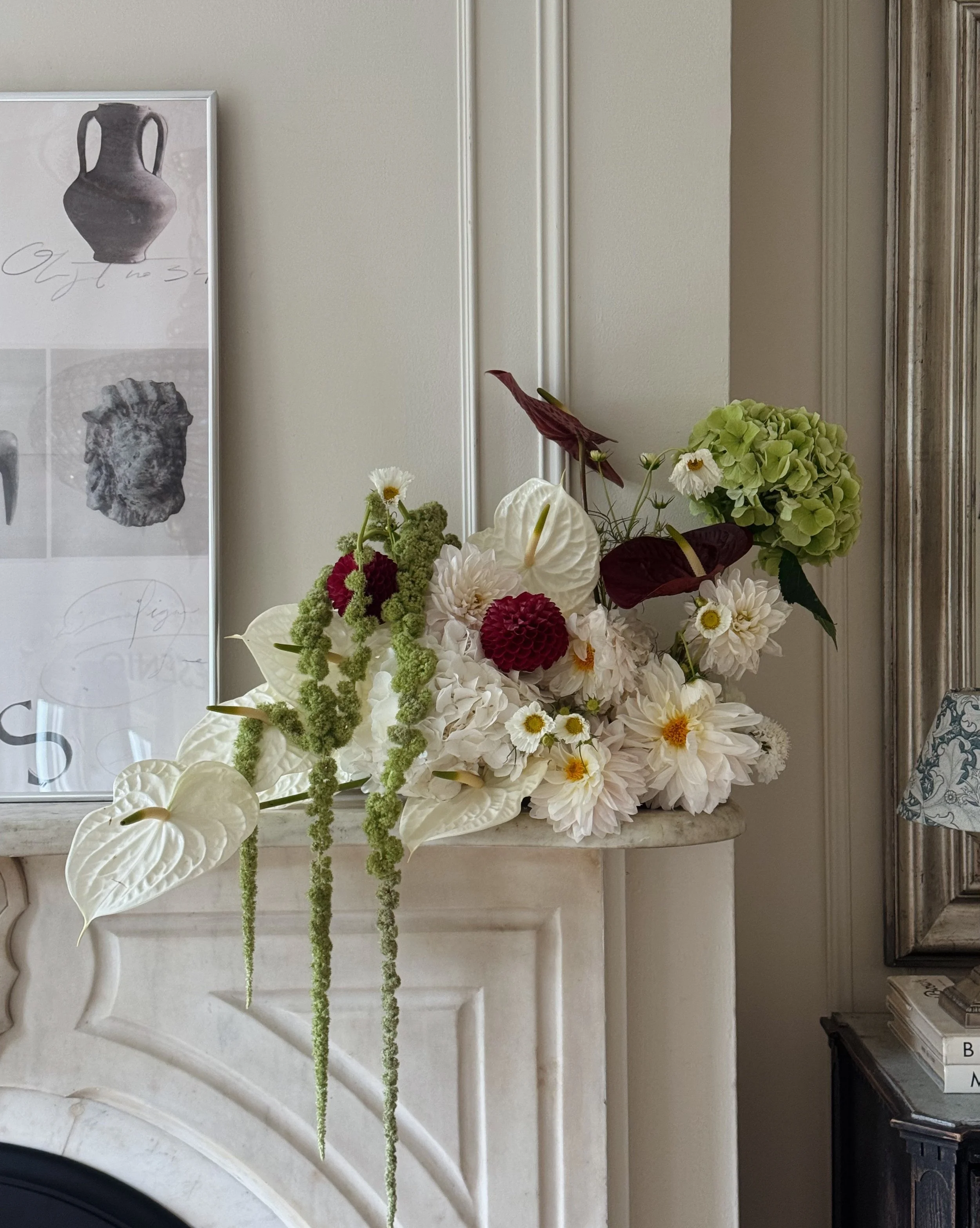 A modern floral arrangement with white and burgundy flowers, including anthuriums and dahlias, placed on a marble fireplace mantle