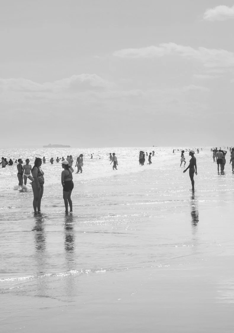 People enjoying their time at the beach, walking and standing in the shallow water under a cloudy sky.