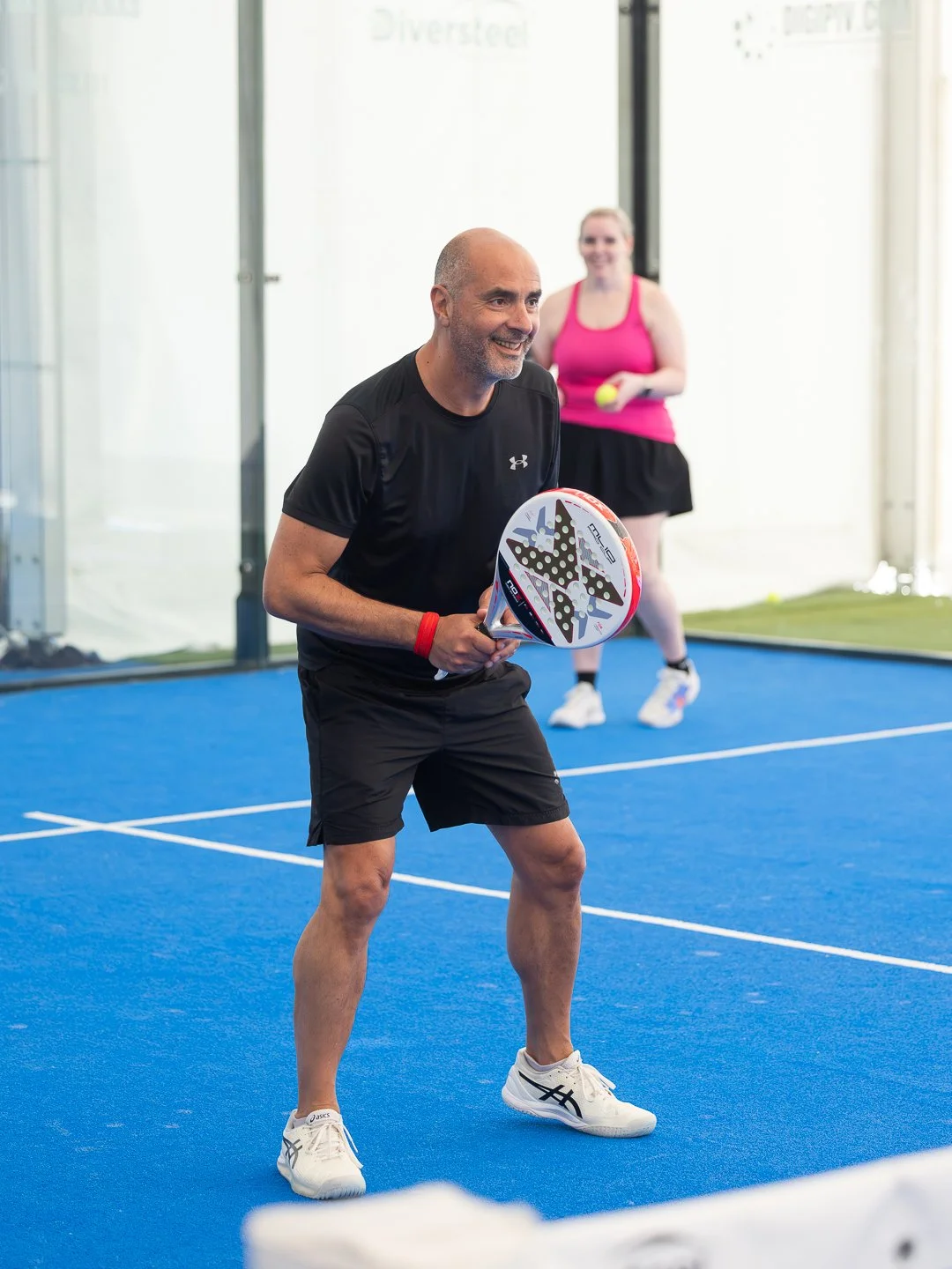 Man playing padel on a blue court holding a red and white racket during padel holiday.