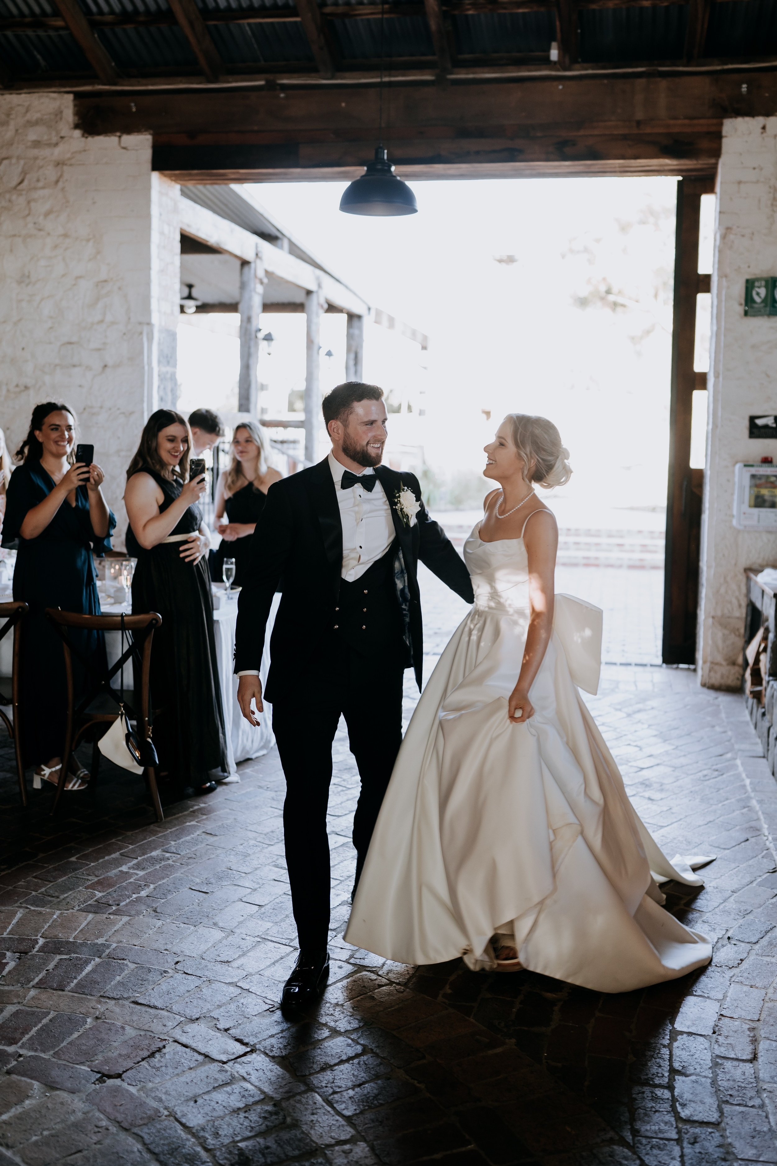 A bride and groom dancing at their wedding reception, with guests watching and taking photos in the background.