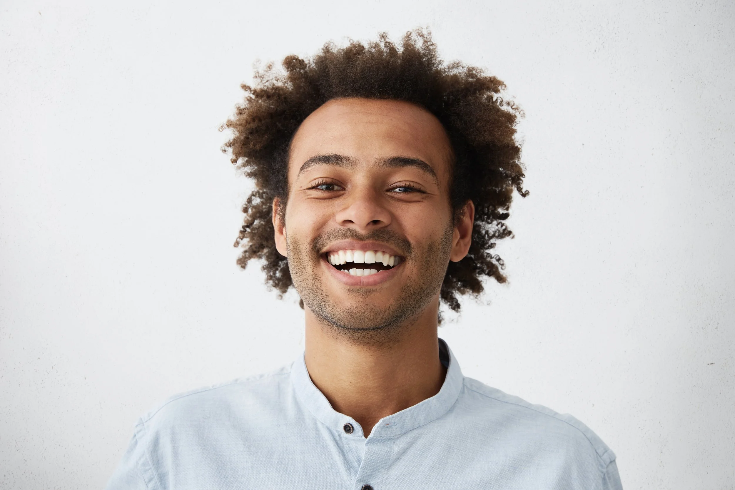 Smiling man with curly hair wearing a light blue shirt against a white background.