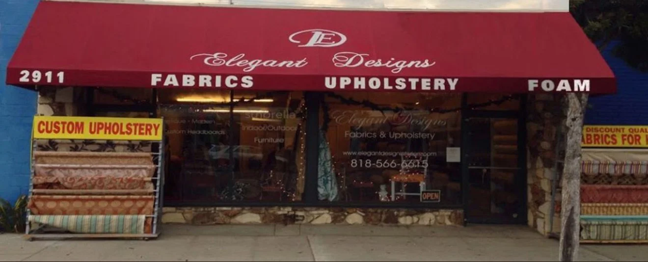 Storefront of Elegant Designs offering fabrics, upholstery, and foam services with signage and fabric rolls displayed.