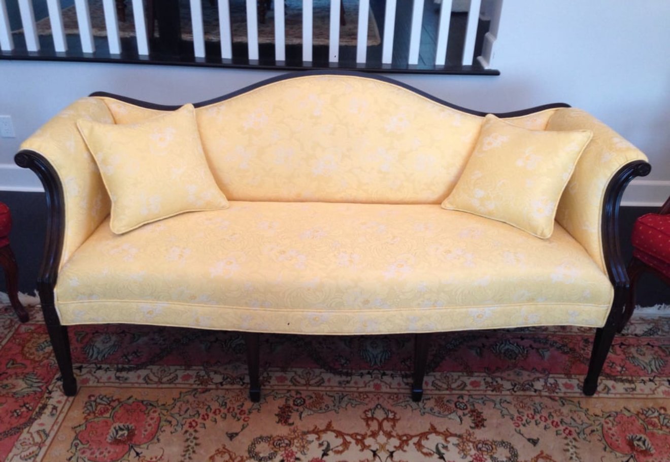Antique sofa loveseat reupholstered in a yellow-cream pattern floral fabric with black wooden frame.