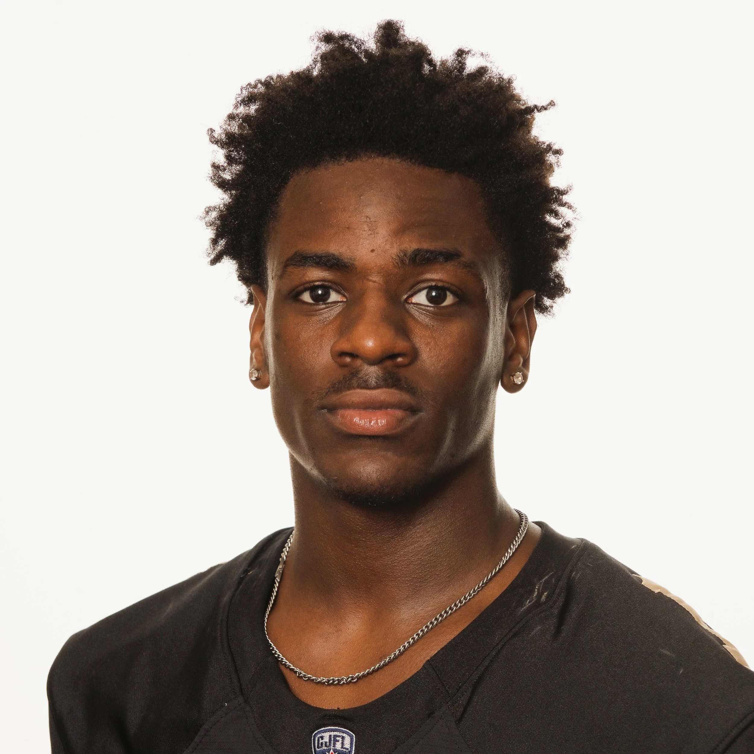 Portrait of a young African American male football player wearing a black Huskies jersey and silver chain.