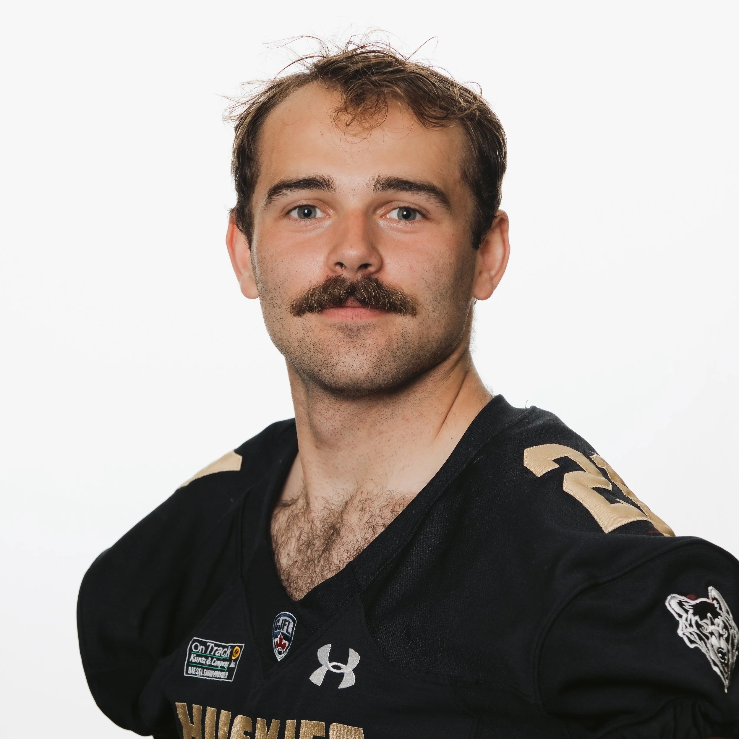 Young male football player in black jersey with 'Huskies' logo, standing against a black background.