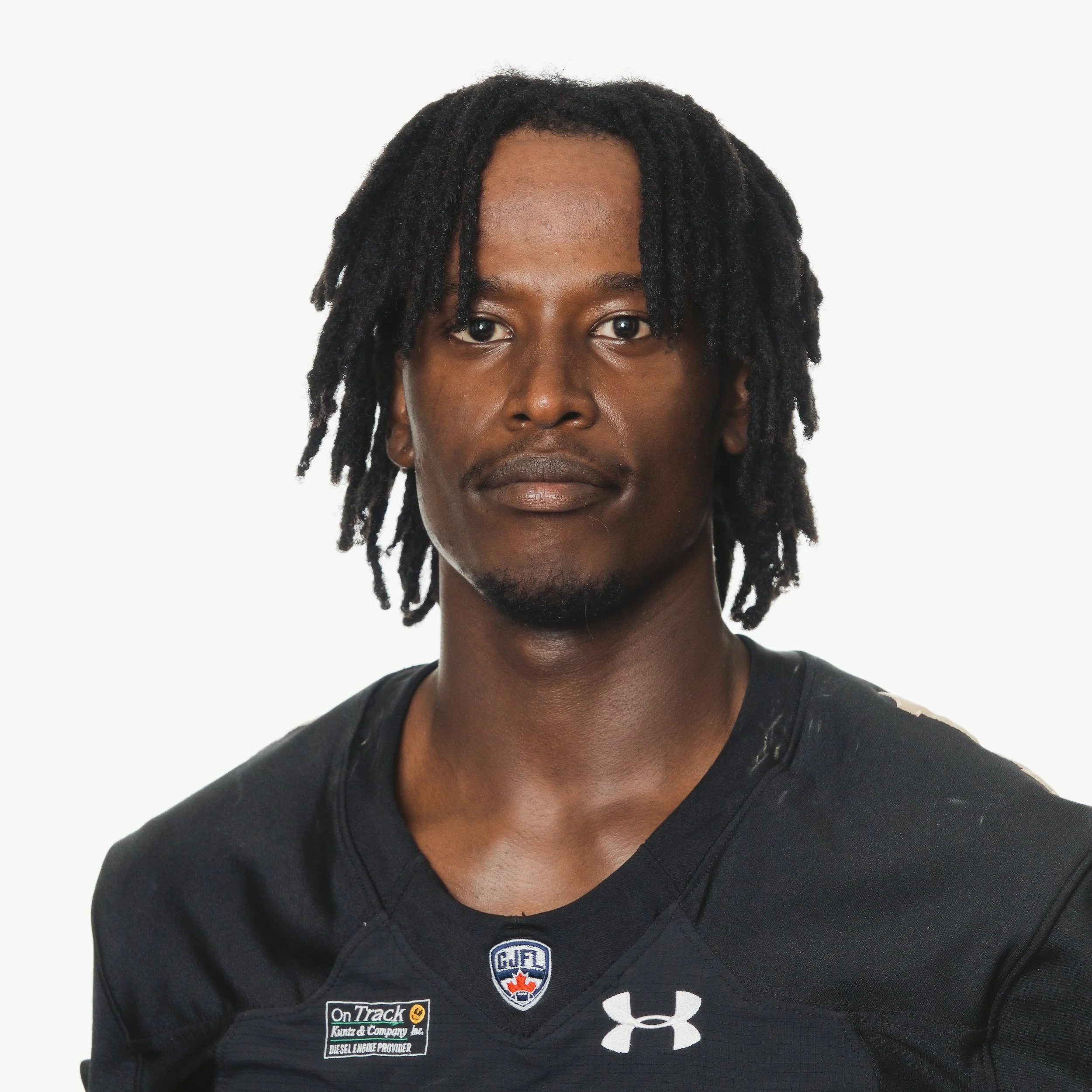 Portrait of a young man with dark skin, wearing a black football jersey with 'HUSKIES' written on it, and earrings.