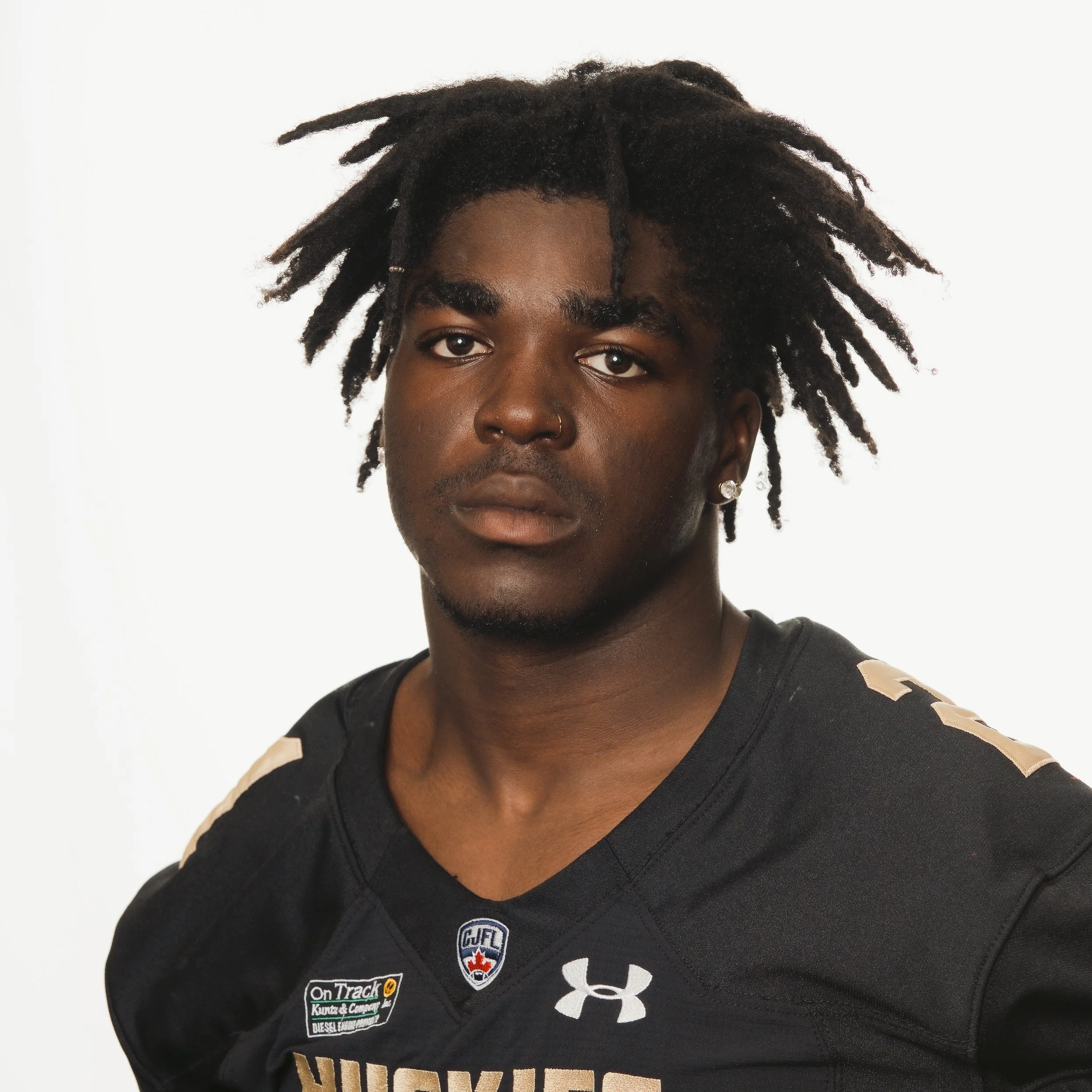 Portrait of a young African American male football player wearing a black Huskies jersey with a GMAC logo.