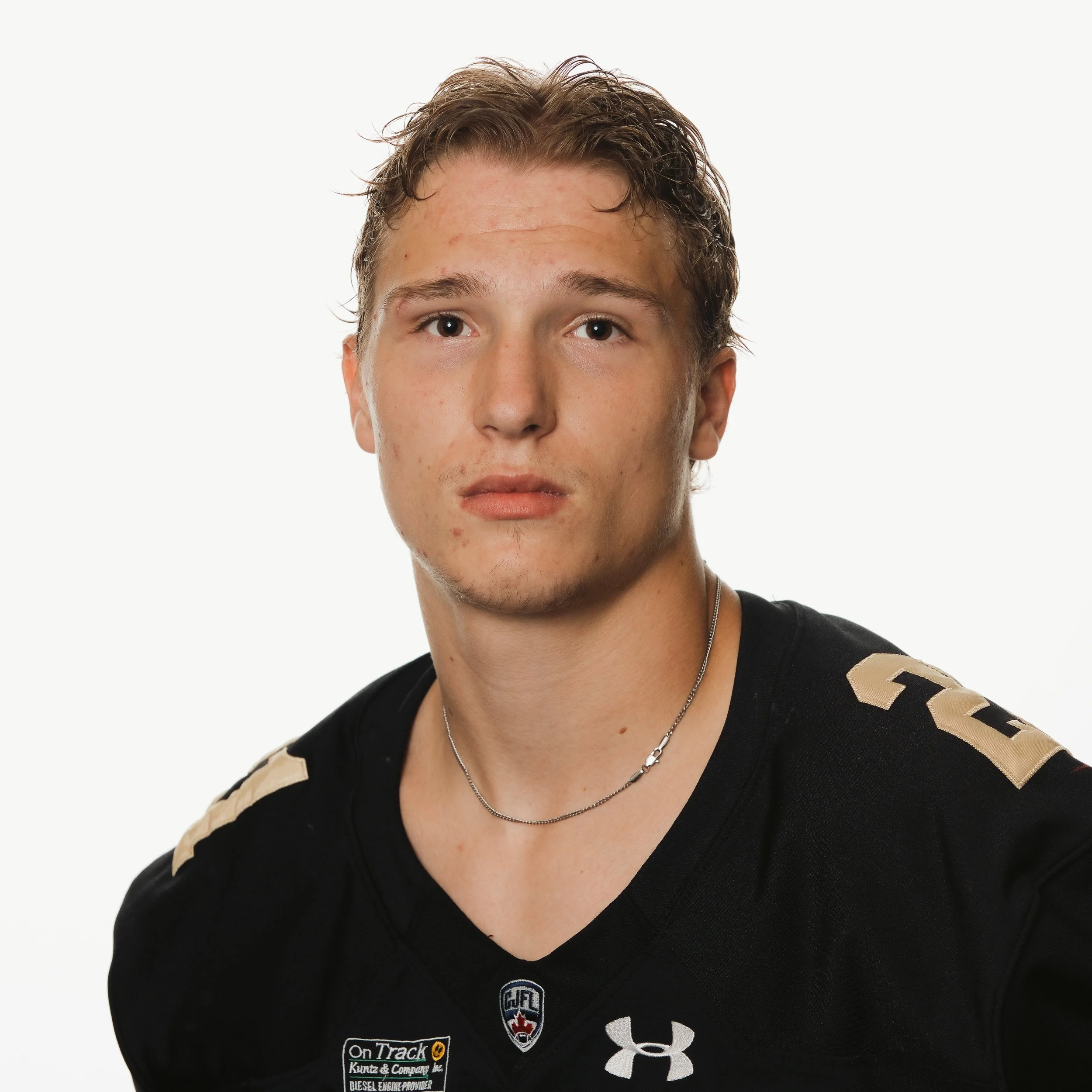 Young male football player in a black jersey with gold accents and the number 98, standing with arms behind back, facing camera against dark background.