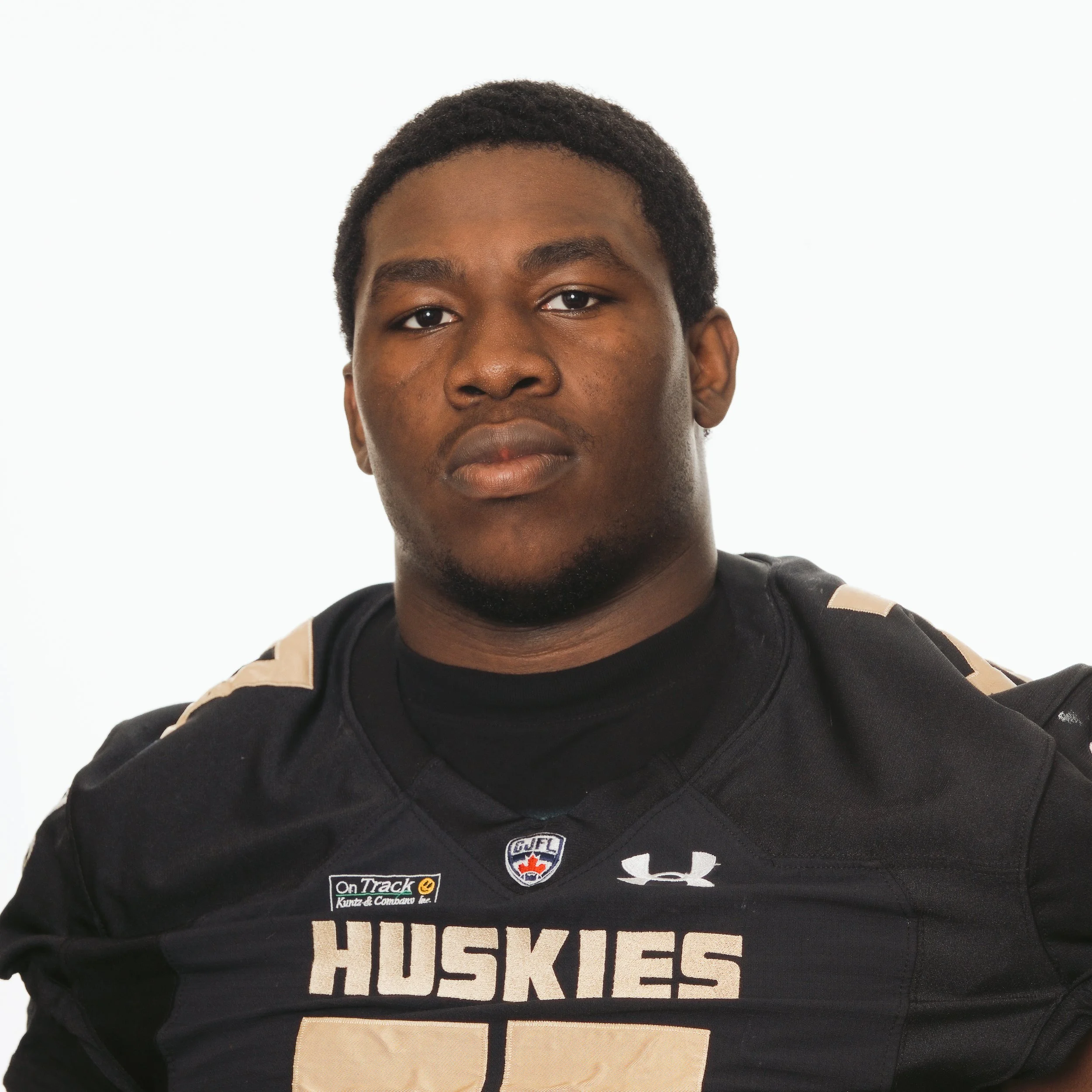 A young African American male football player in a black jersey with 'HUSKIES' written on it, wearing a serious expression.