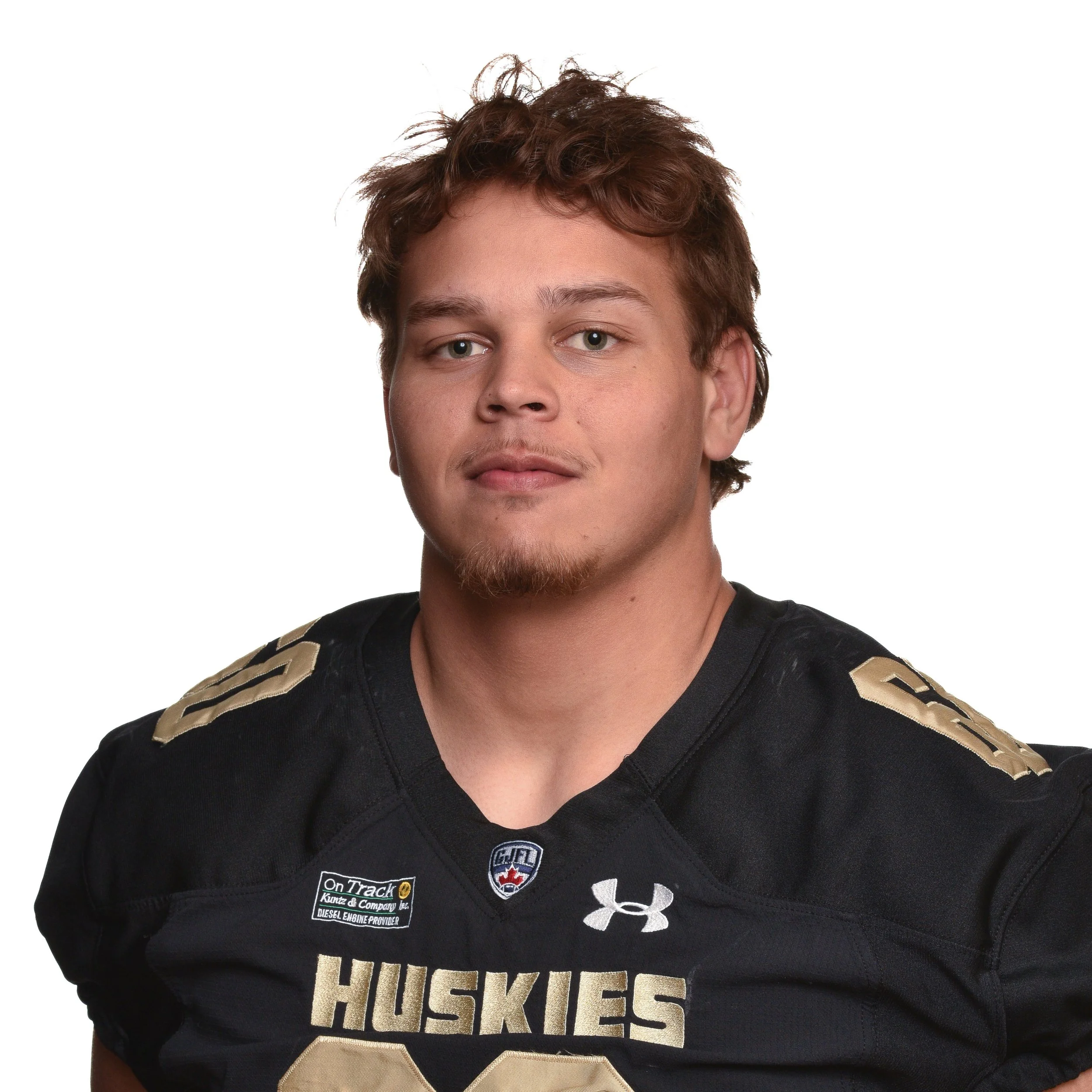 A young man with light skin and brown hair in a football jersey with 'Huskies' printed on it, standing against a white background.