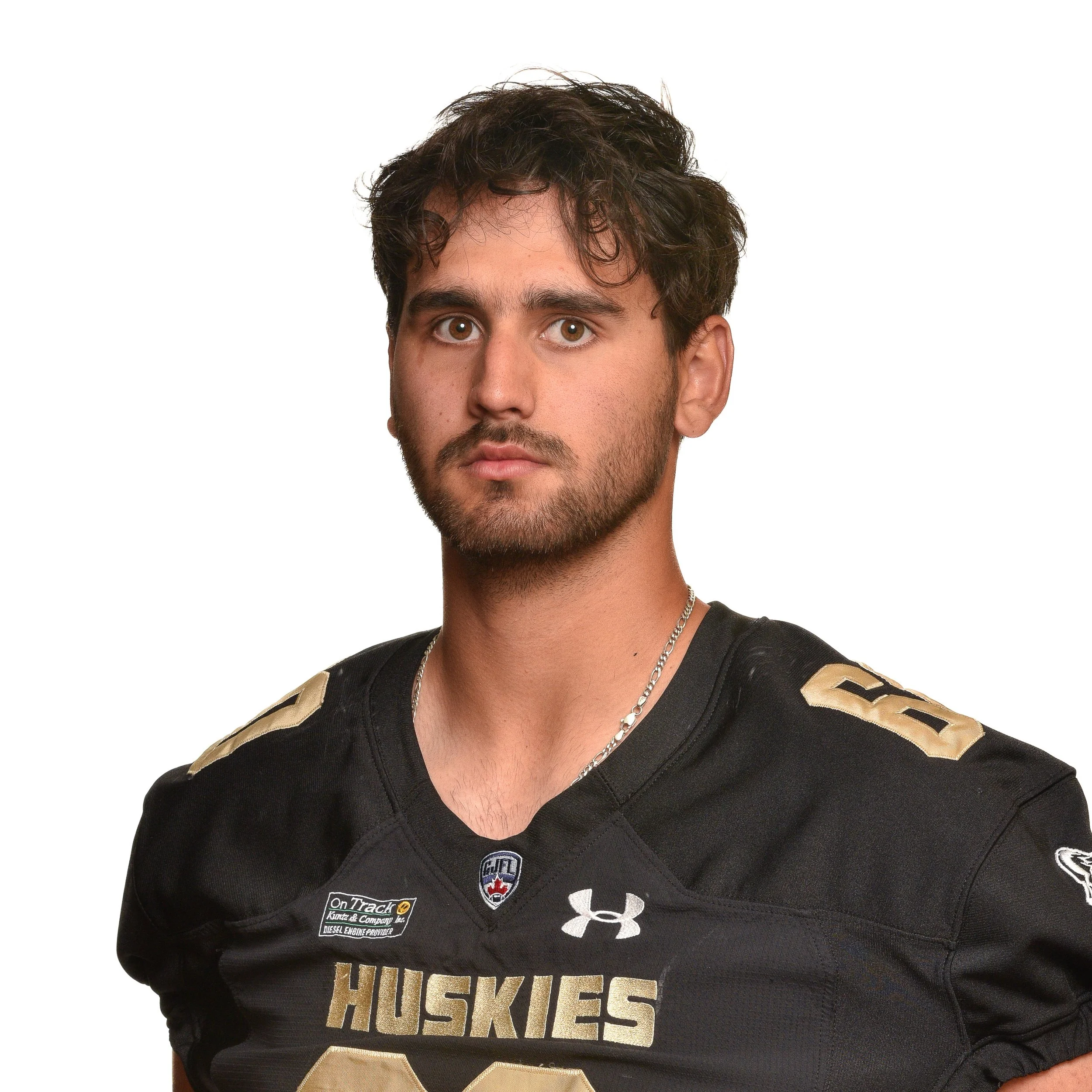 A young male football player in a black Huskies jersey with the number 56, standing against a white background.