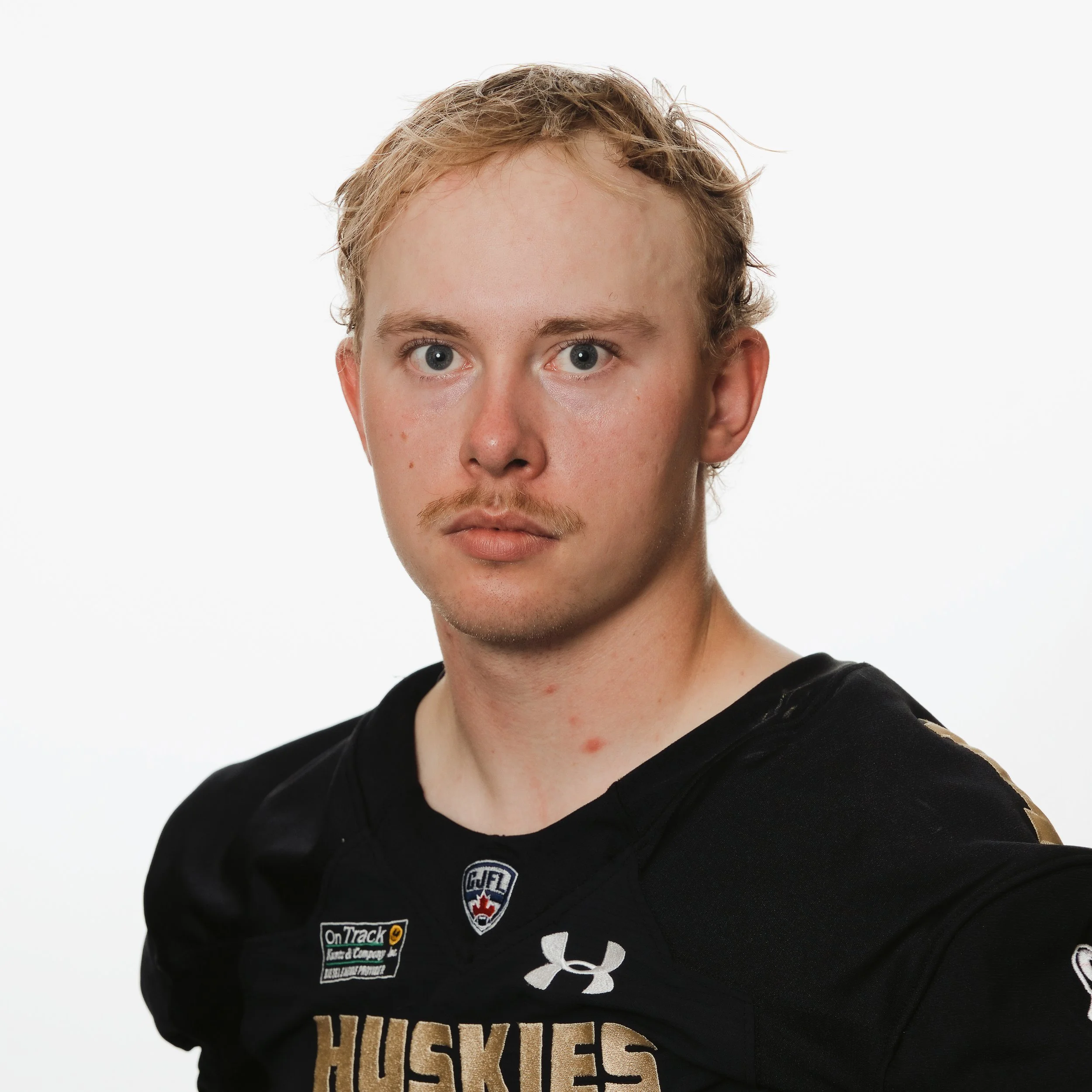 A young man with short, light-colored hair wearing a black football jersey with 'Huskies' written on it, standing against a white background.